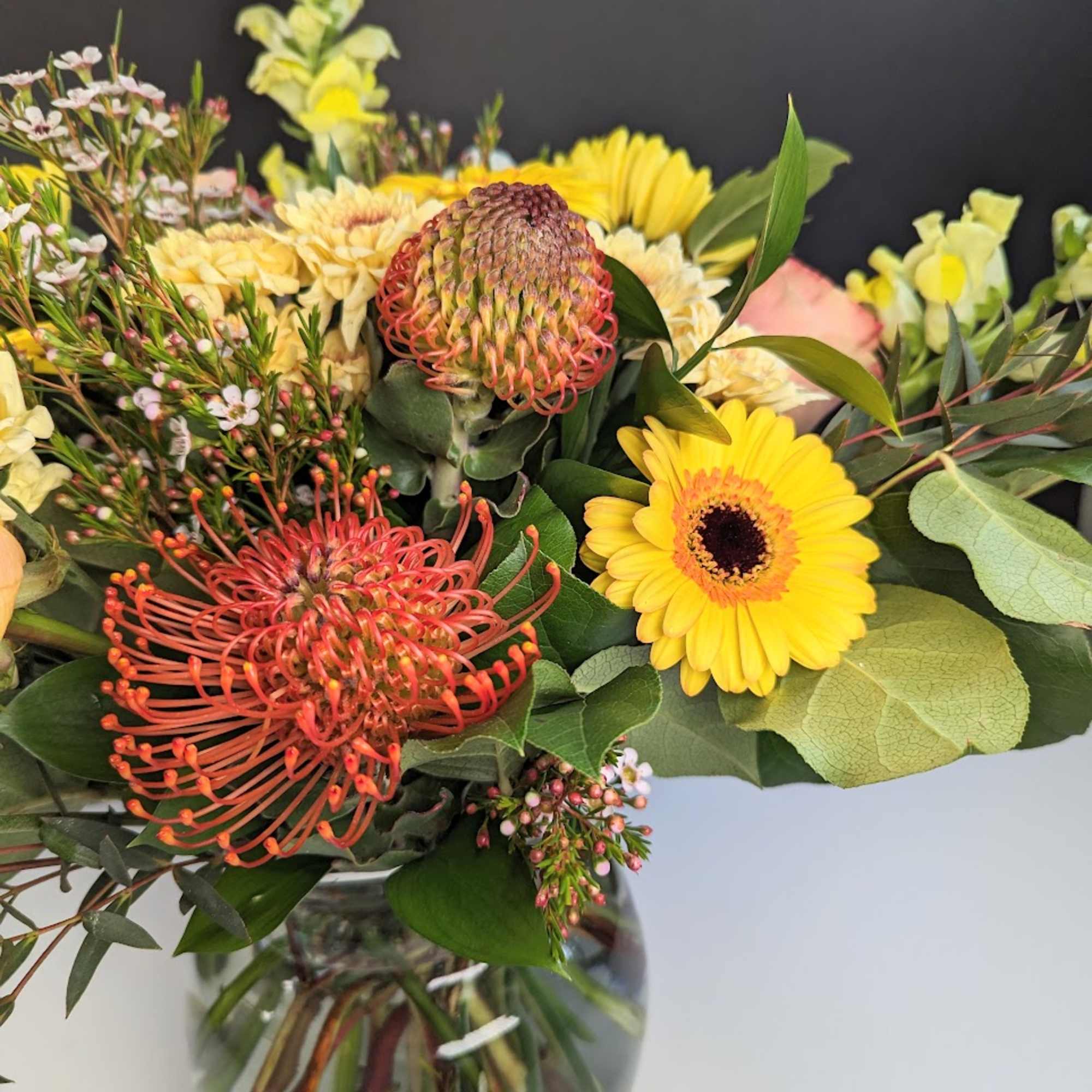 Bouquet with yellow gerbera daisies and orange pincushion protea in a glass vase