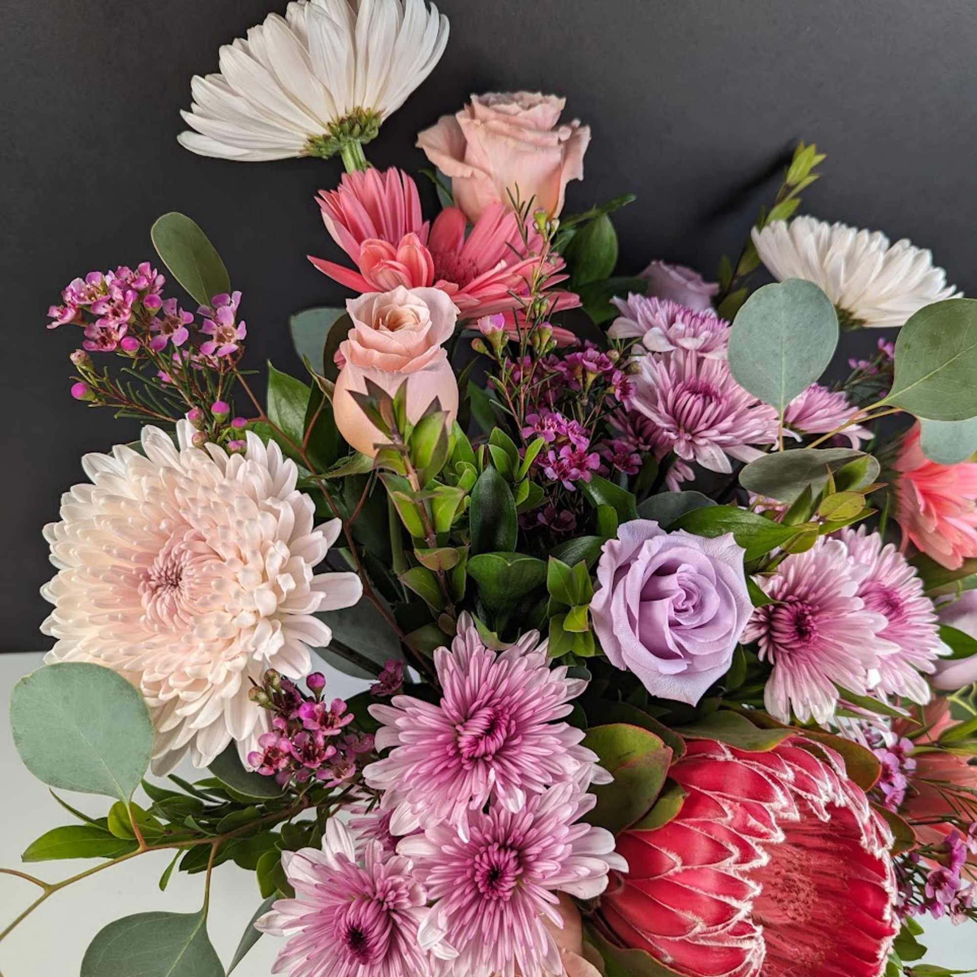 Bouquet of pink, white, and lavender flowers with a red protea