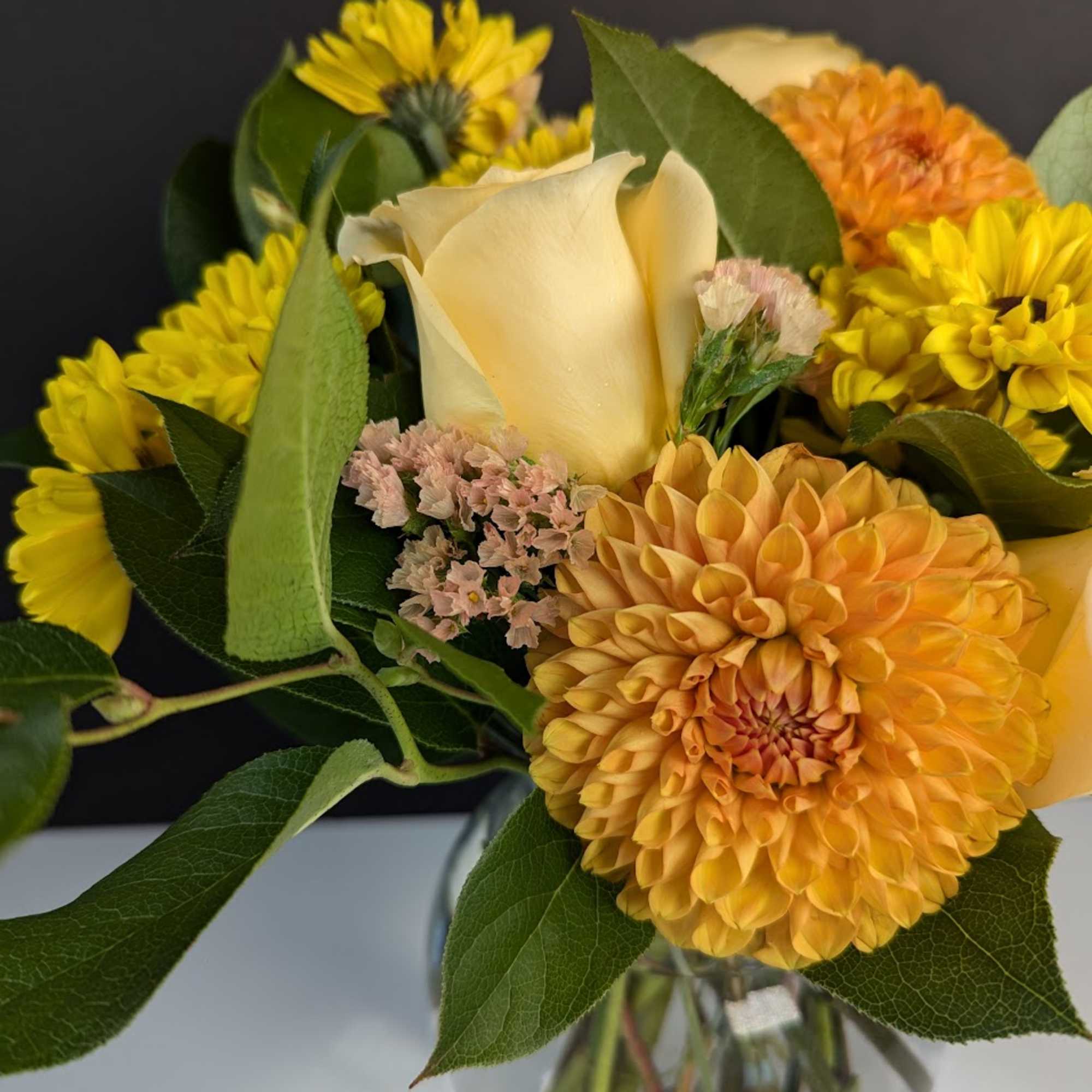 Bouquet of yellow and orange flowers with a cream calla lily in a glass vase
