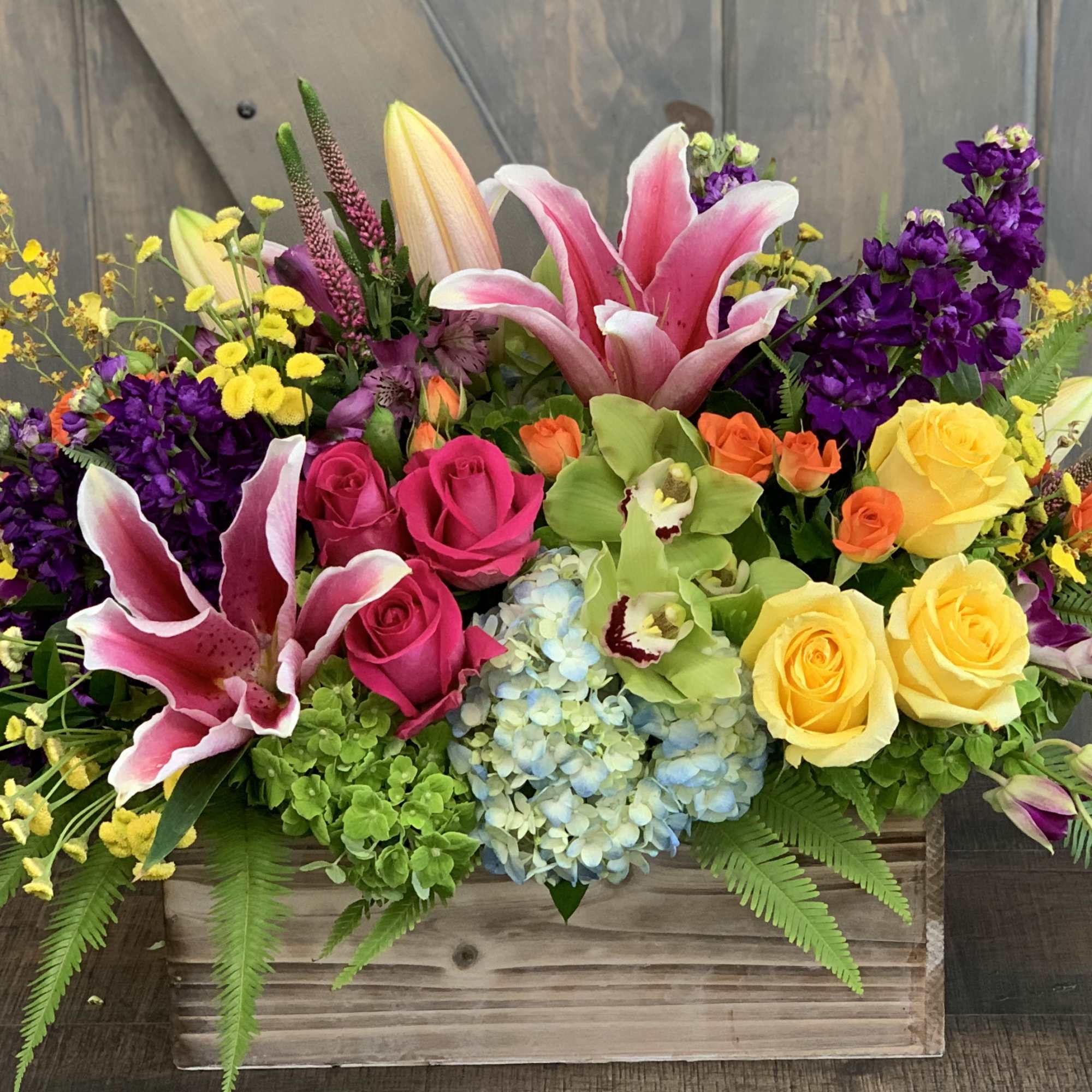 Colorful mixed flower arrangement in a wooden box with roses and lilies
