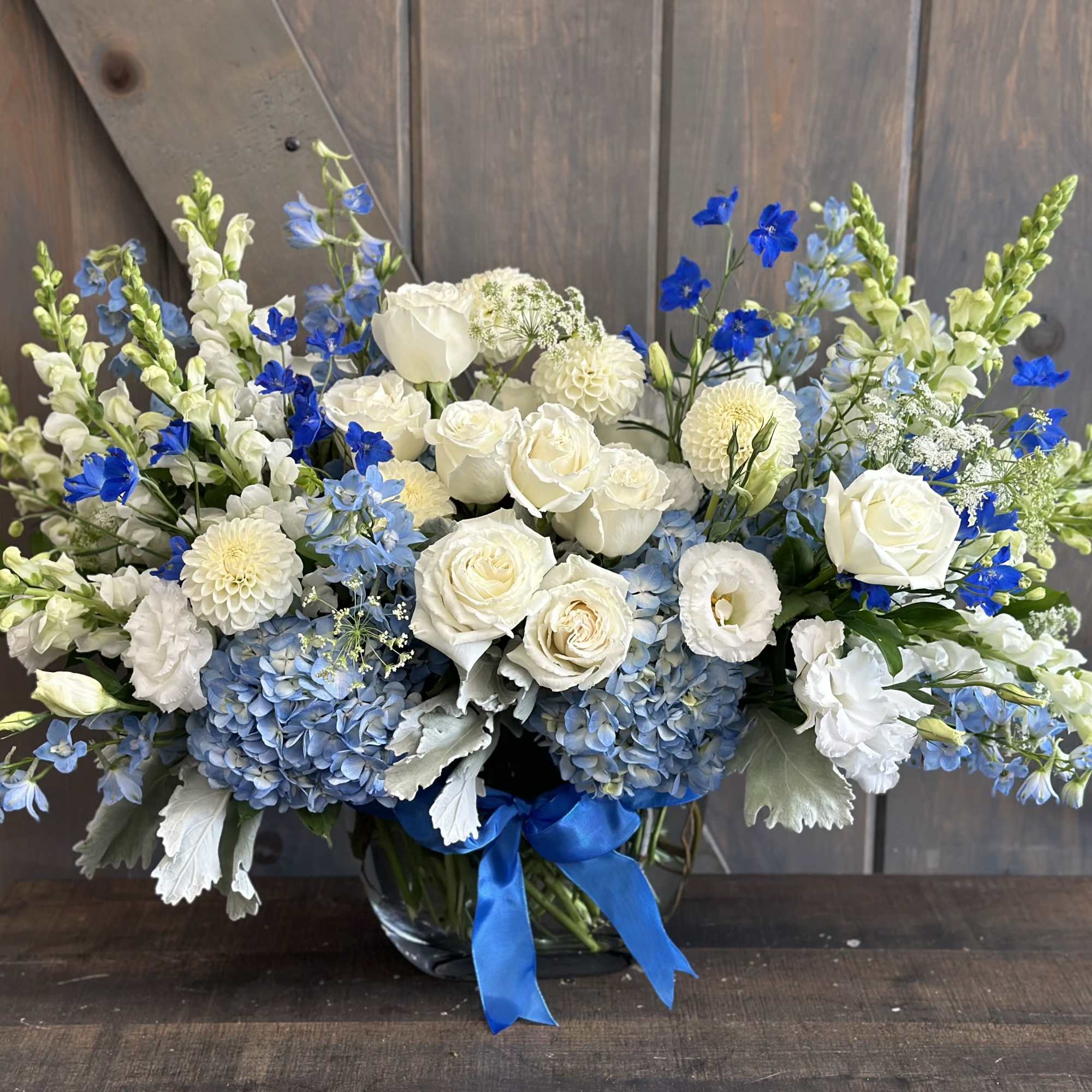 Blue and white floral arrangement in a glass vase with a blue ribbon