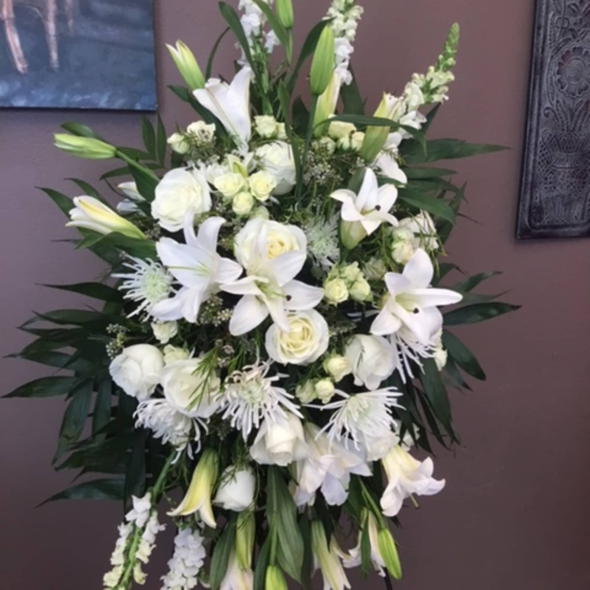 White floral standing spray with lilies and roses on a black easel