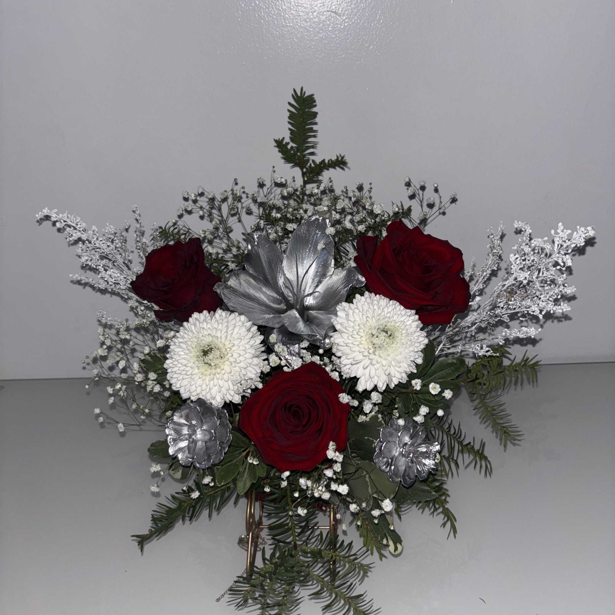 Red roses and white daisies with silver accents in a compact arrangement