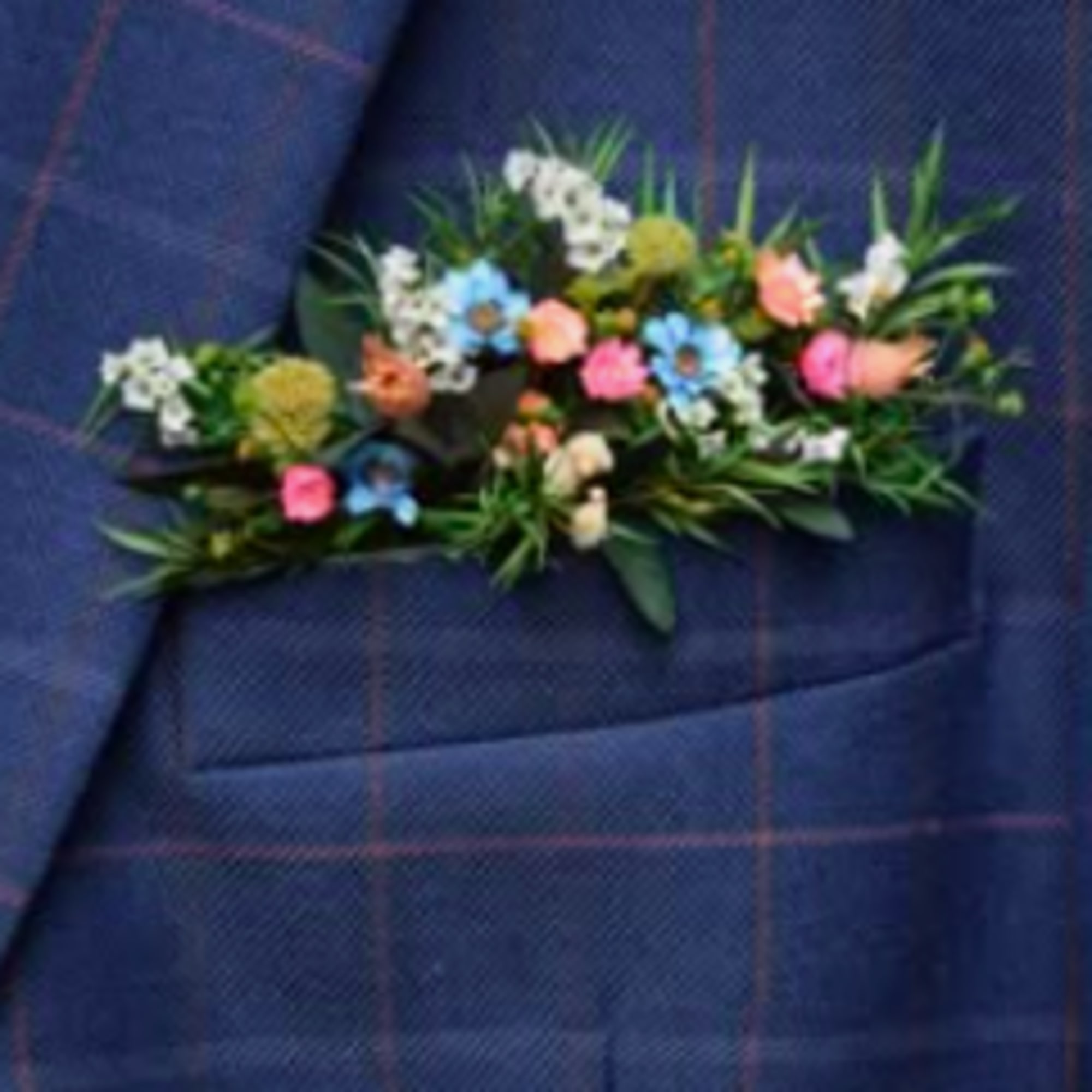 Small floral boutonniere with pastel blooms on blue plaid fabric