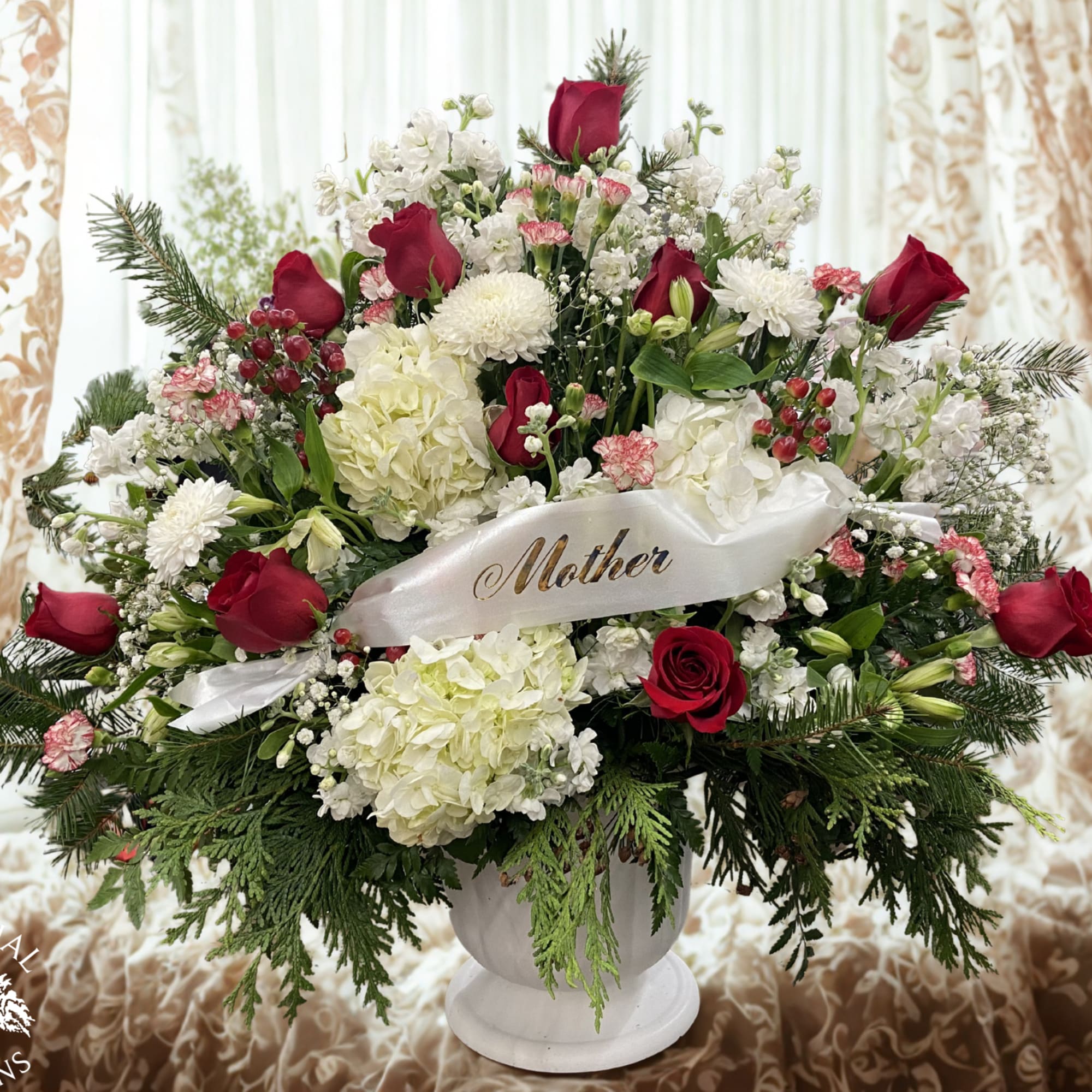 Large red and white floral arrangement in a white vase with a Mother ribbon