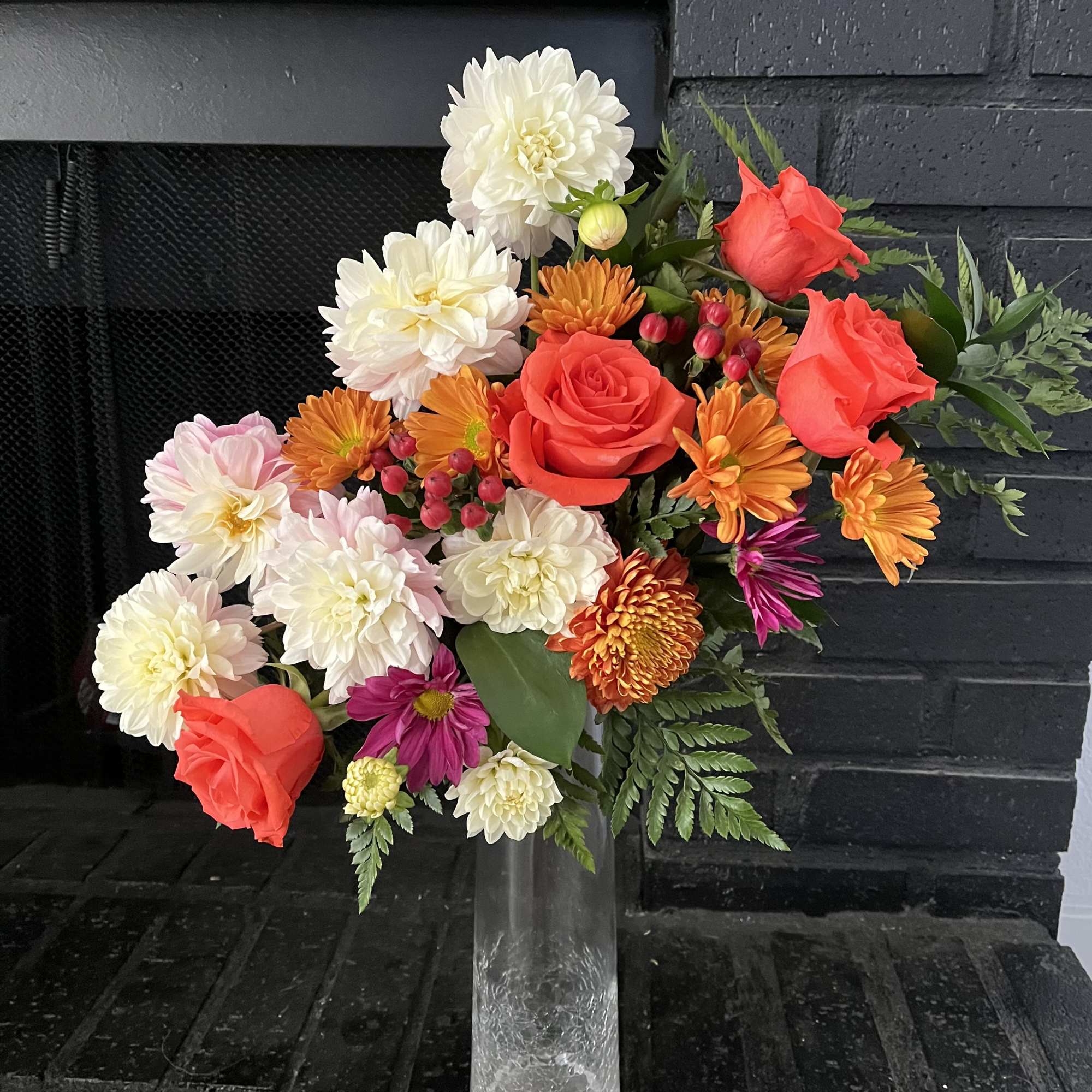 Mixed bouquet of red roses, white dahlias, and orange blooms in a clear vase