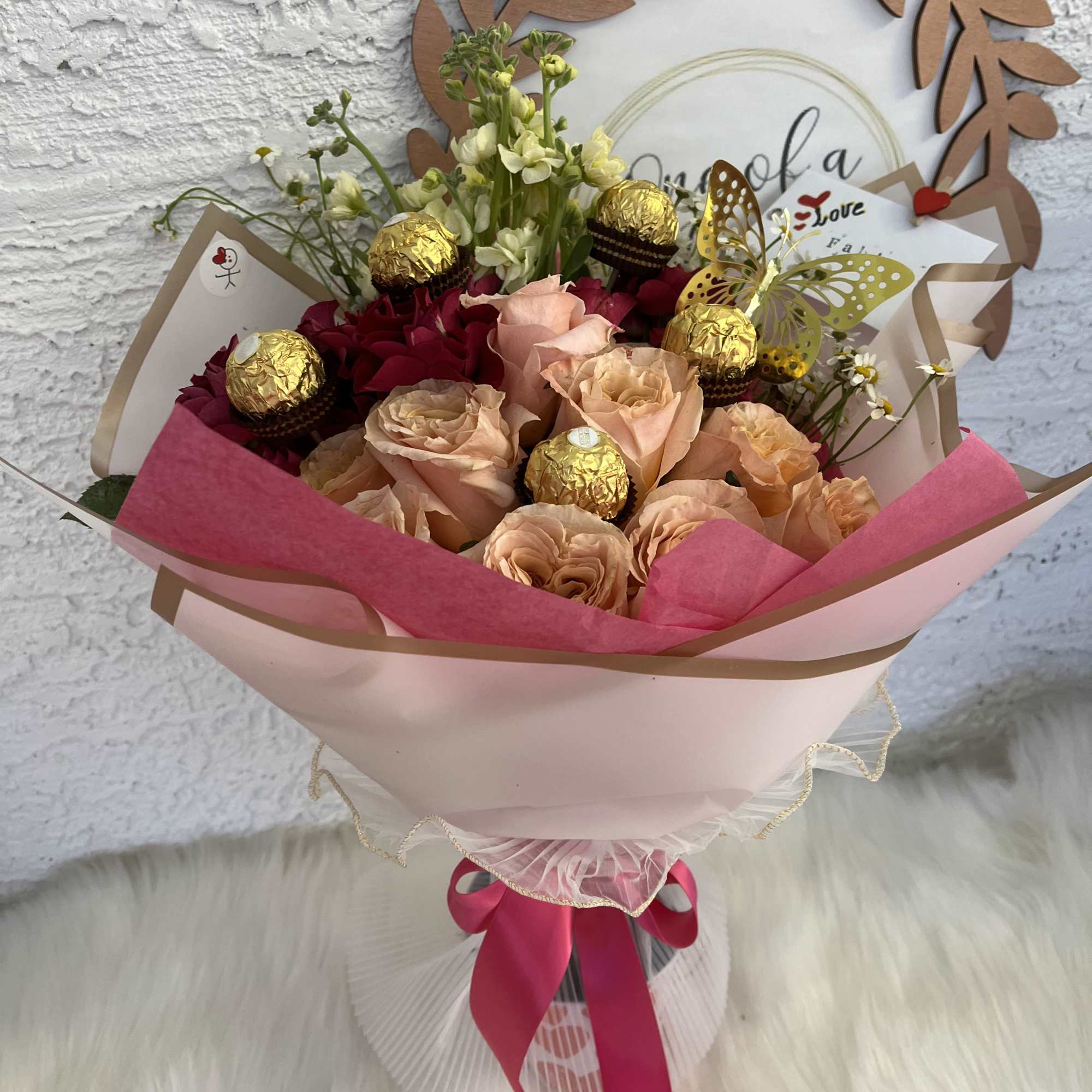 Bouquet of peach and red roses with gold chocolates and a butterfly topper
