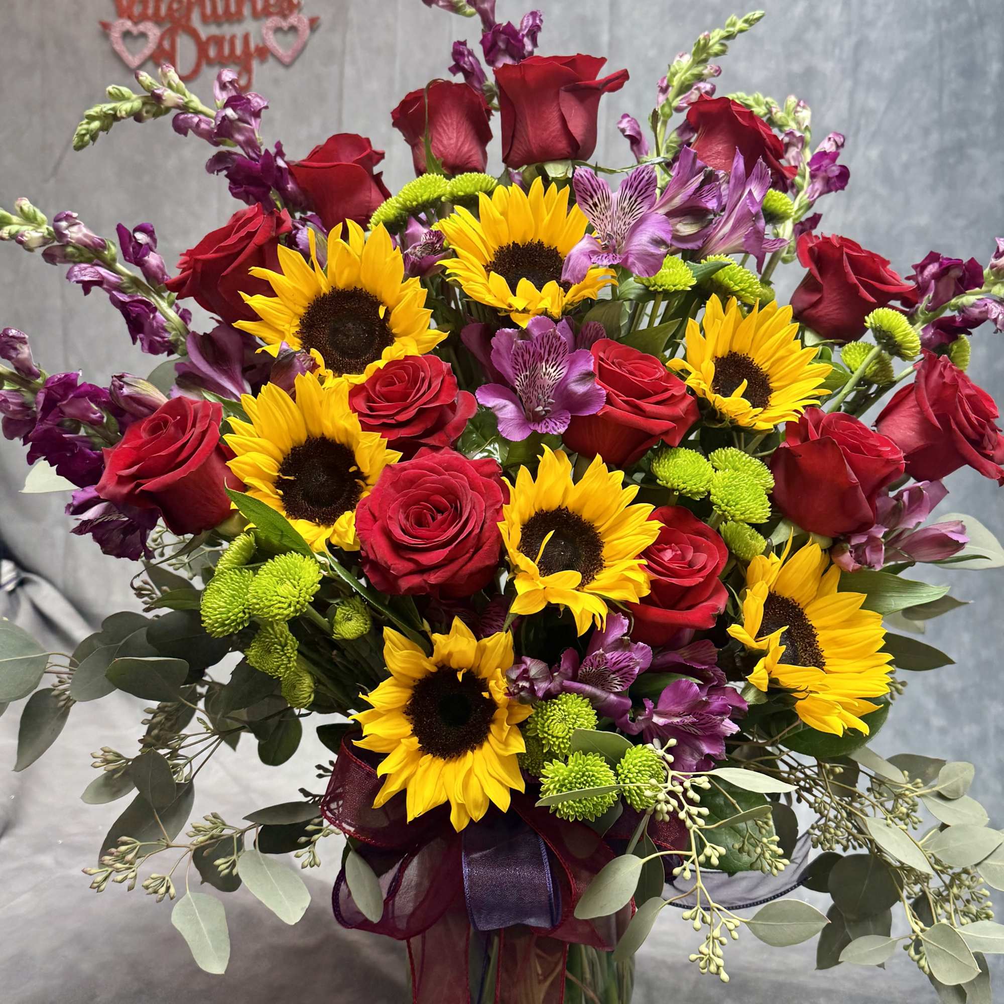 Bouquet of red roses, sunflowers, and purple flowers in a glass vase