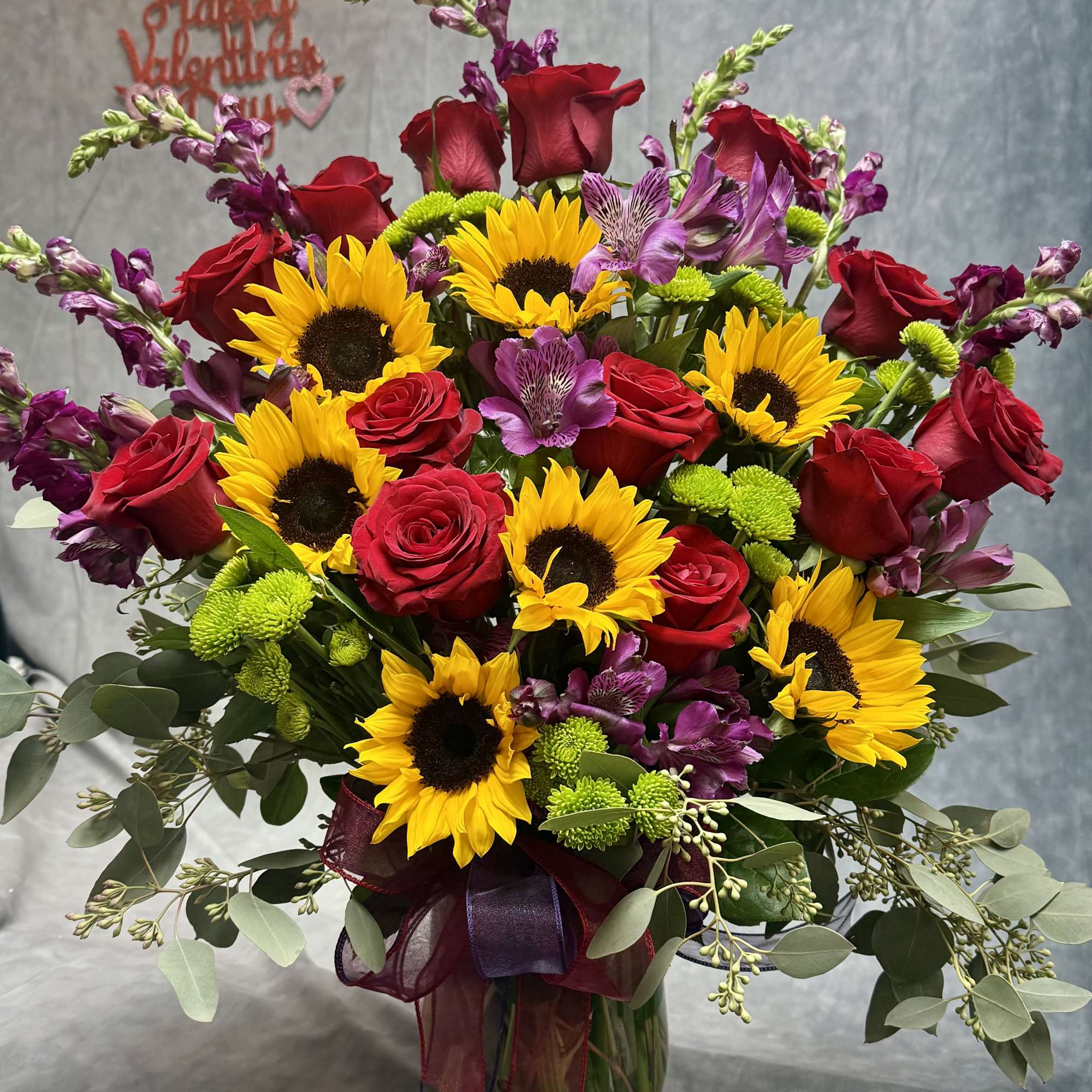 Bouquet of red roses, sunflowers, and purple blooms in a glass vase