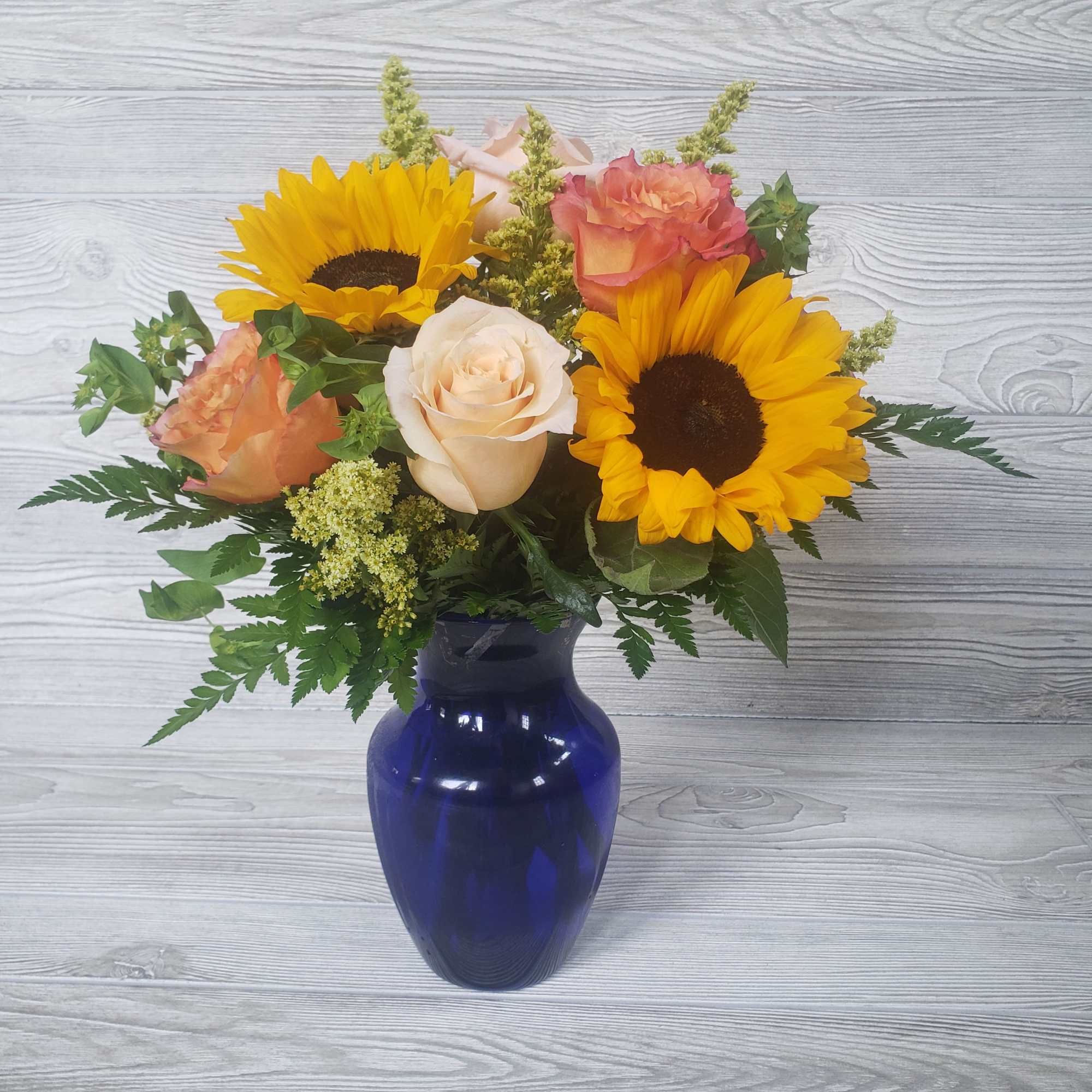 Sunflowers, Roses, Filler in a beautiful cobalt blue vase. 