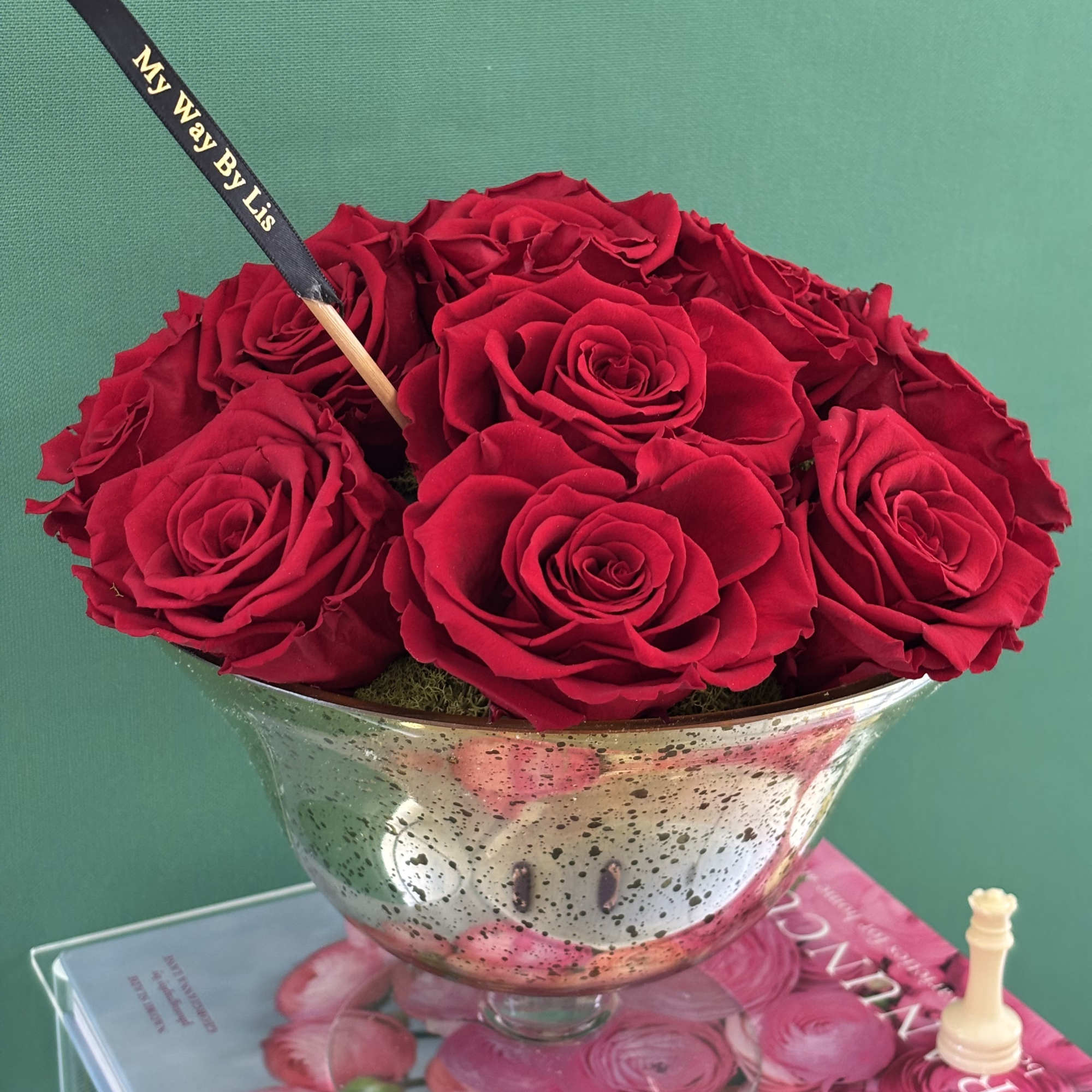 Red roses arranged in a silver pedestal bowl with a black ribbon pick