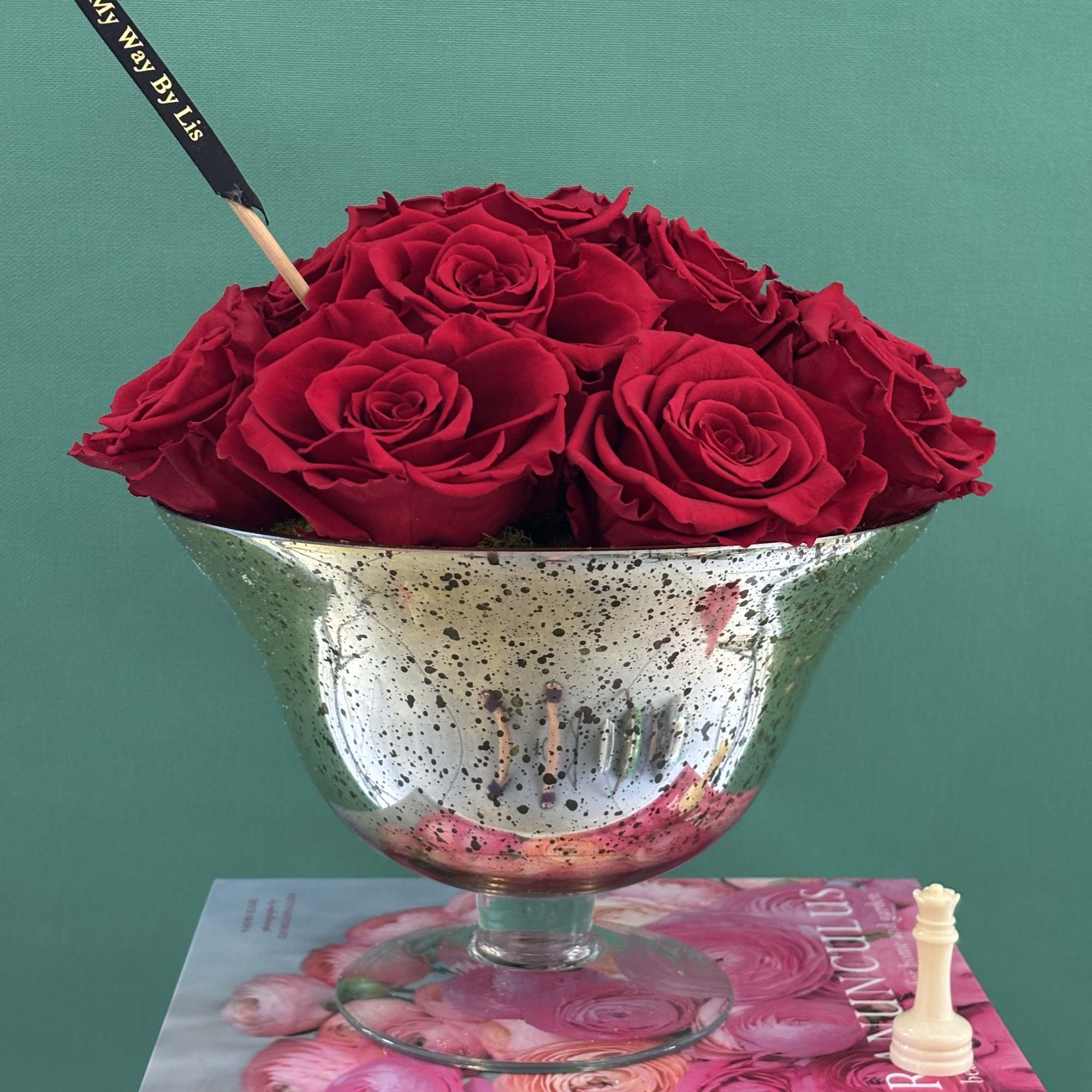 Red roses arranged in a silver pedestal bowl with a small flag pick
