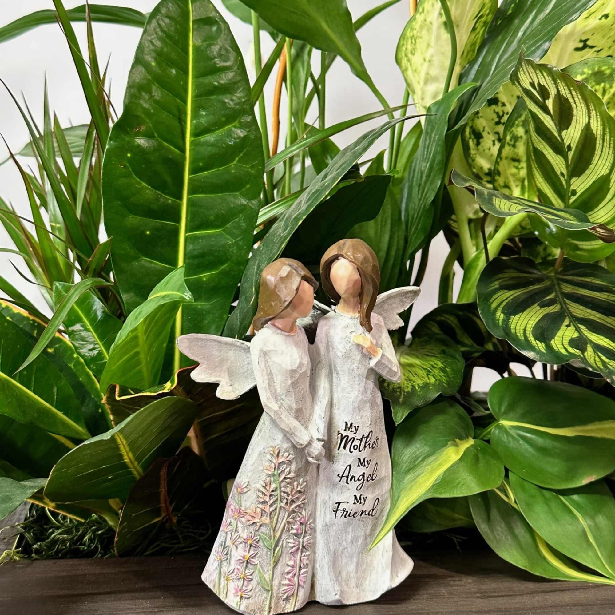 Angel figurine in front of a leafy green plant arrangement