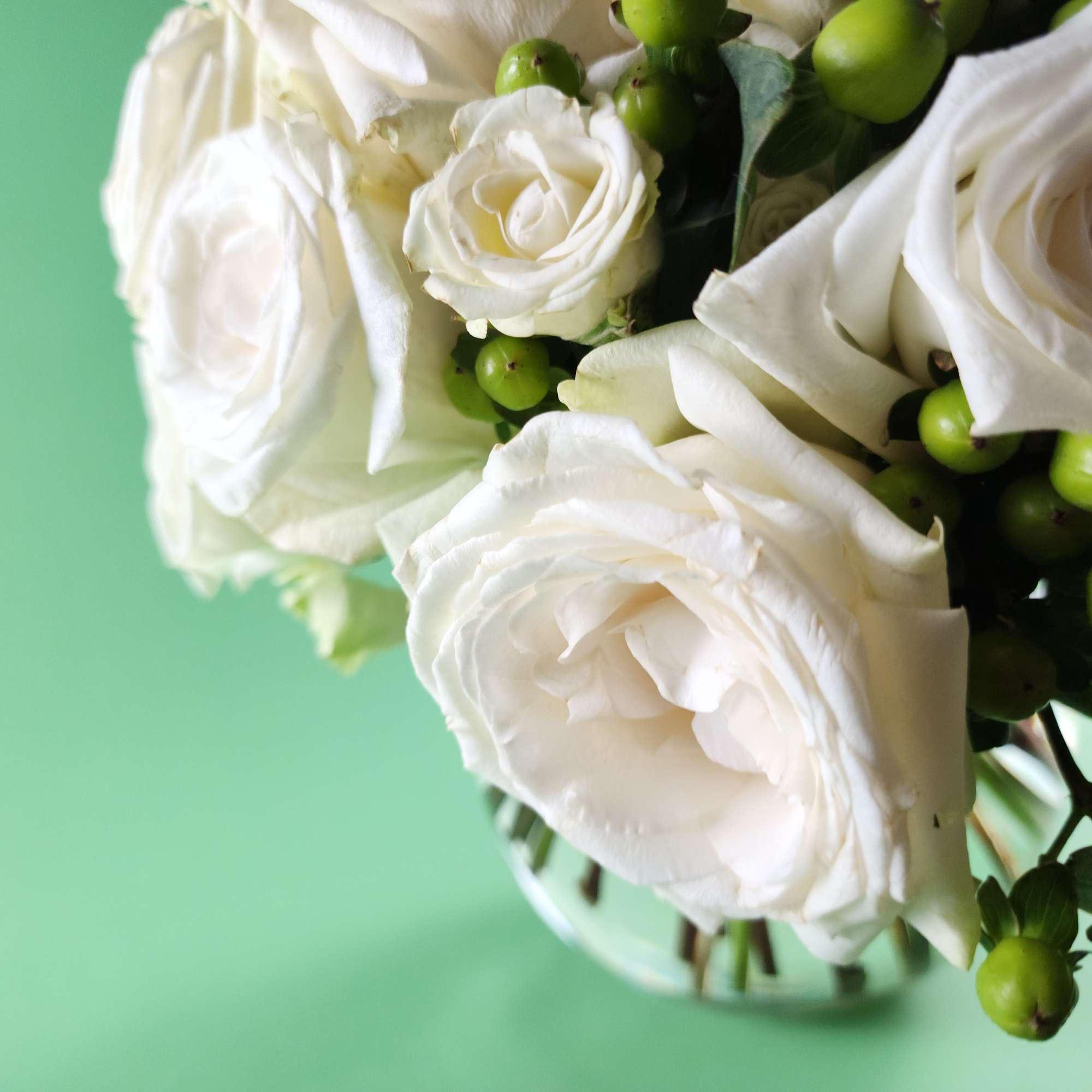 White roses arranged with green berries in a glass vase