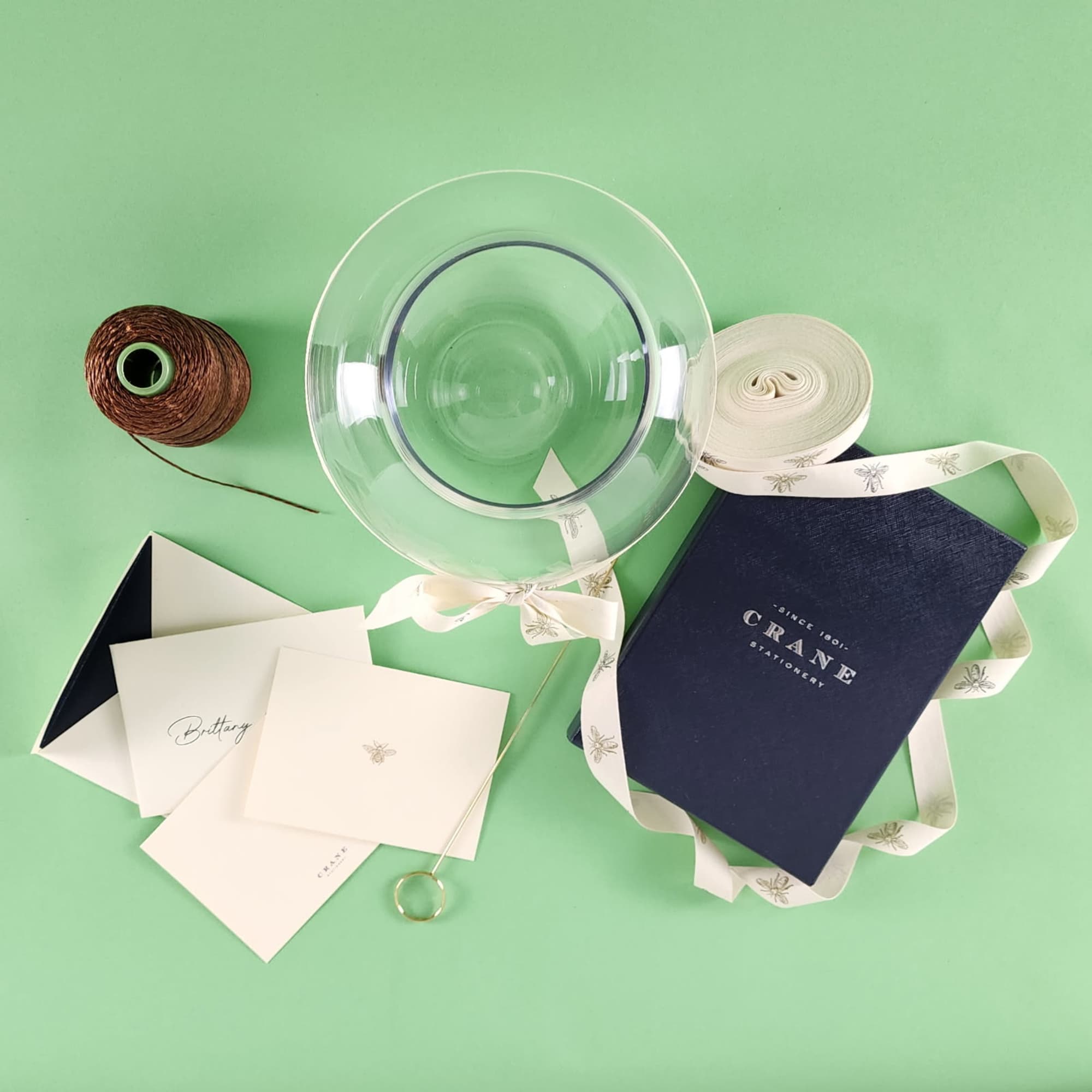 Gift set with a clear glass bowl, ribbon, cards, and a navy box on a green background