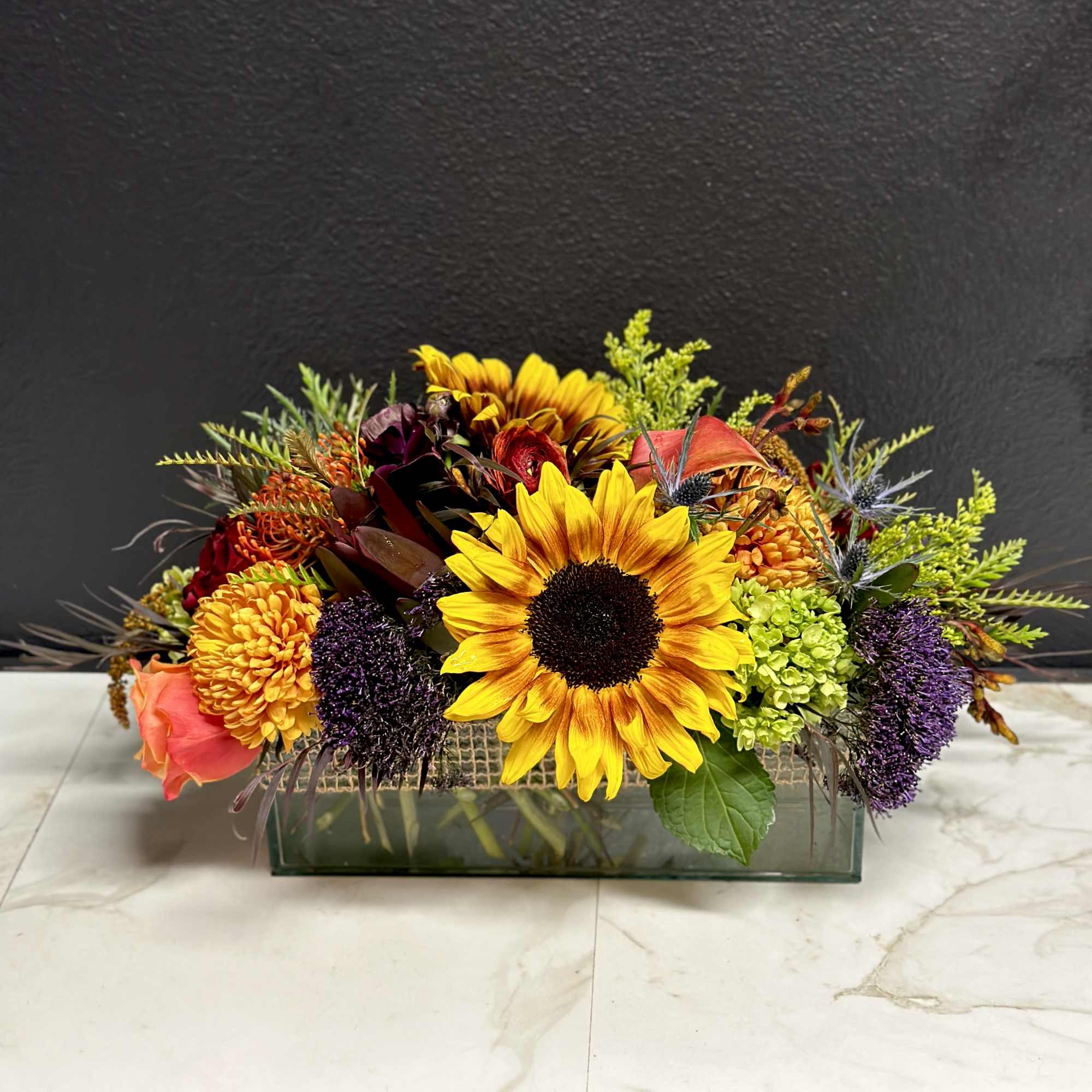 Mixed bouquet with sunflowers, roses, and chrysanthemums in a rectangular glass vase