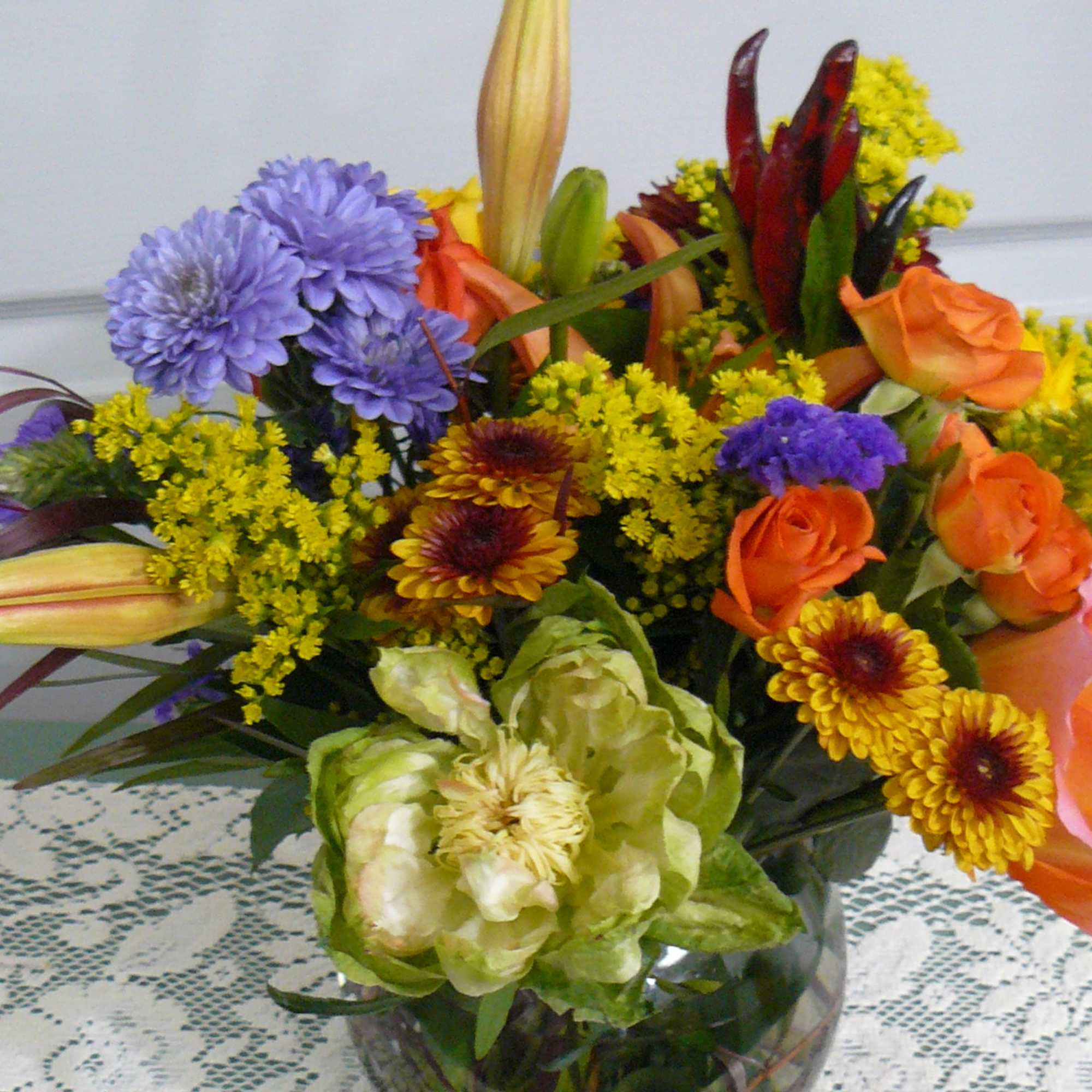 Mixed bouquet with orange roses, purple mums, and lilies in a glass vase