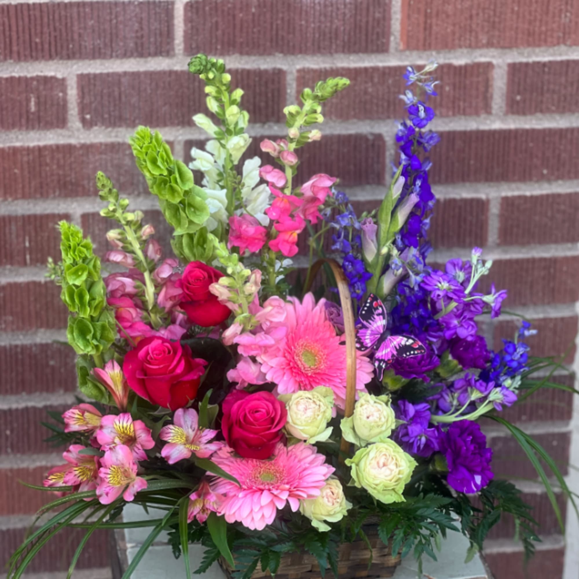 Basket arrangement of pink, purple, and red flowers with a butterfly pick