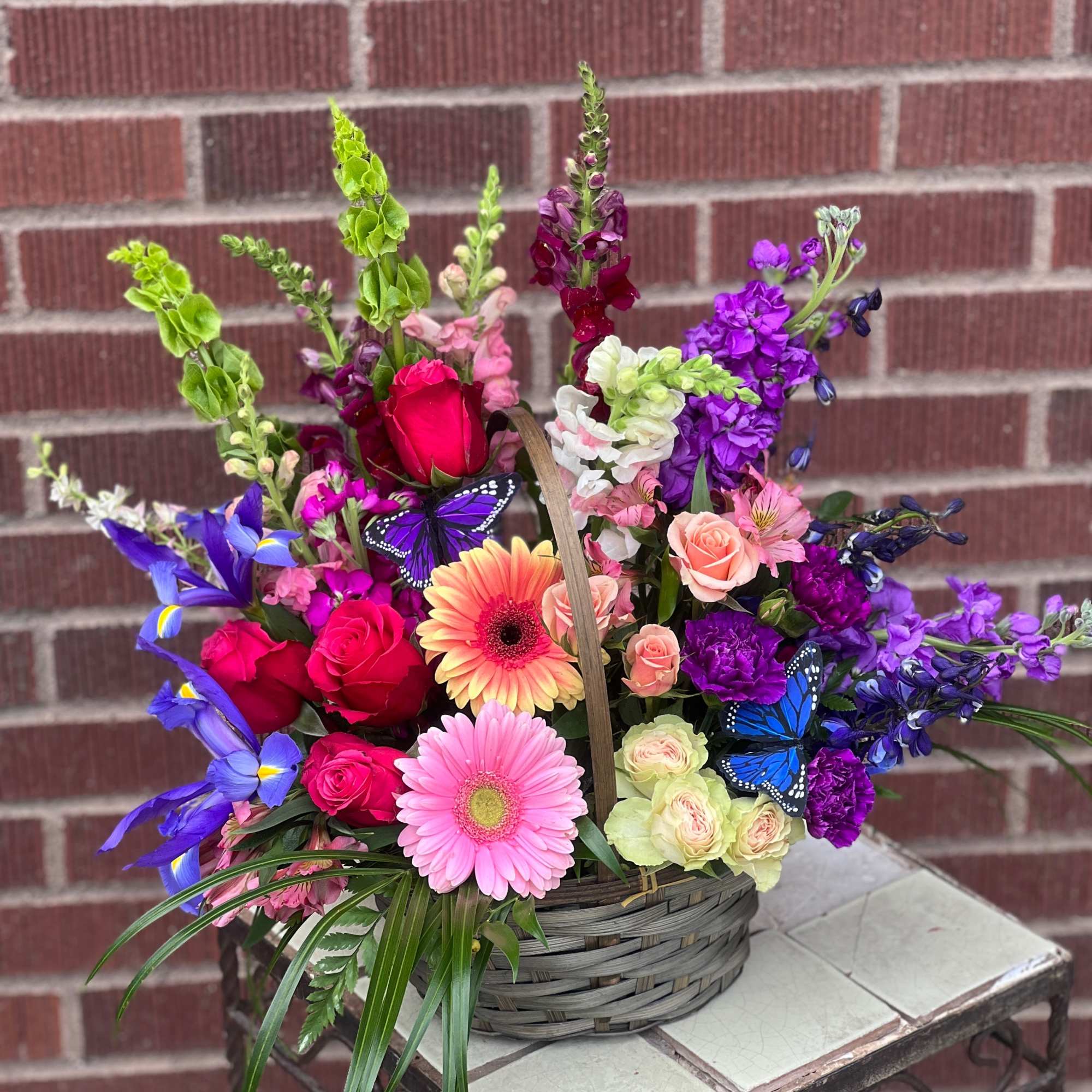 Basket arrangement with roses, gerbera daisies, and purple blooms