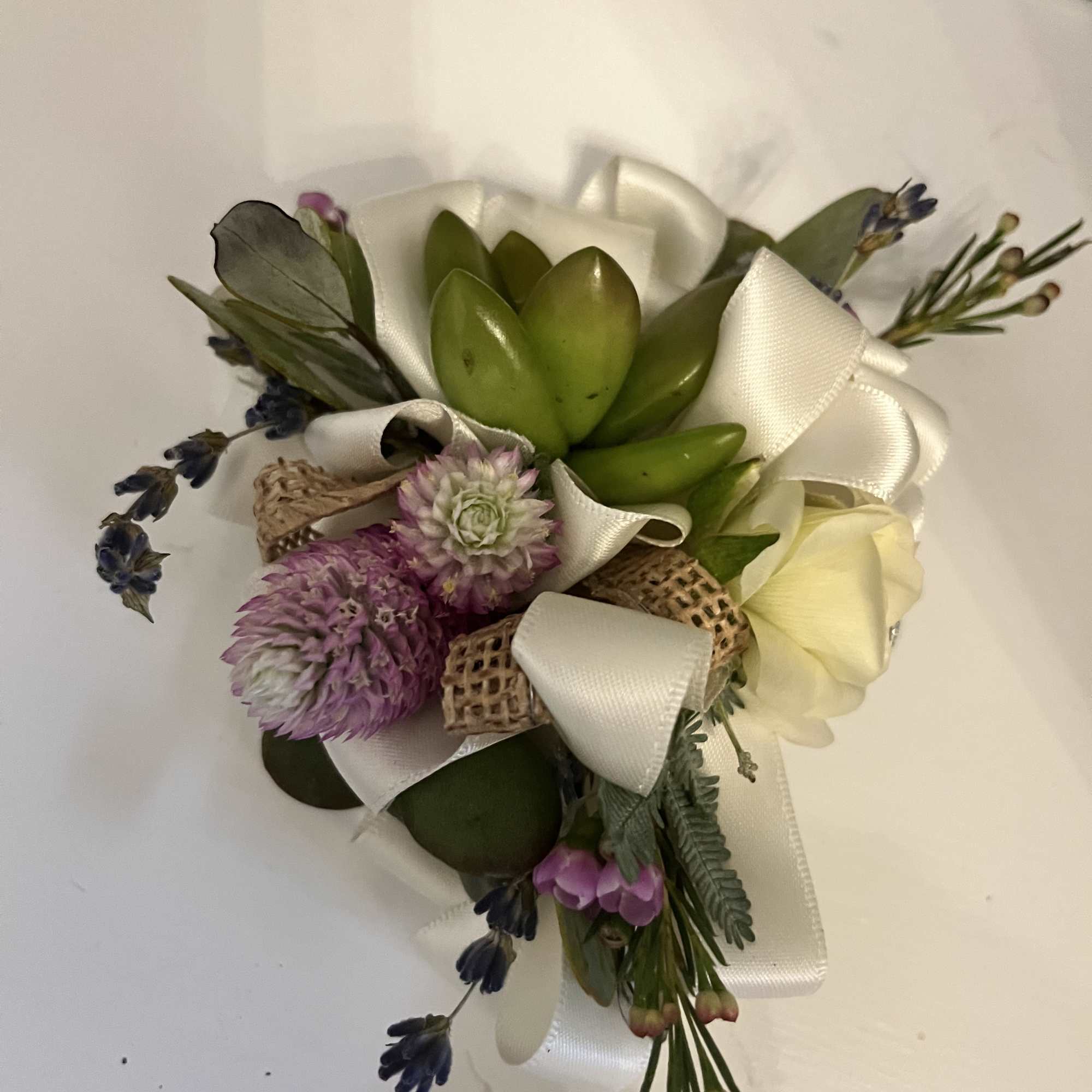 Small boutonniere with succulents, purple flowers, and white ribbon
