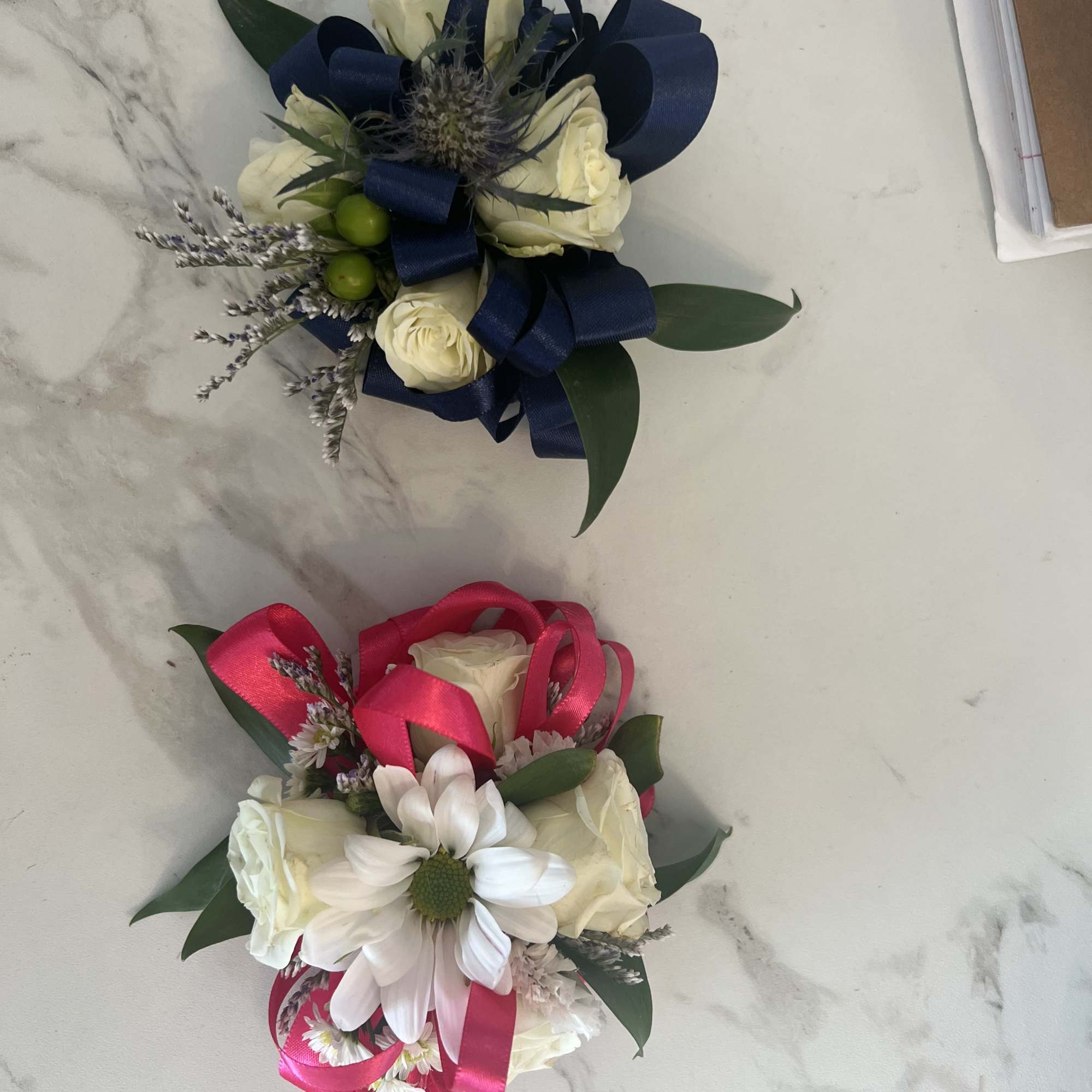 Two small floral corsages with white roses and ribbon accents