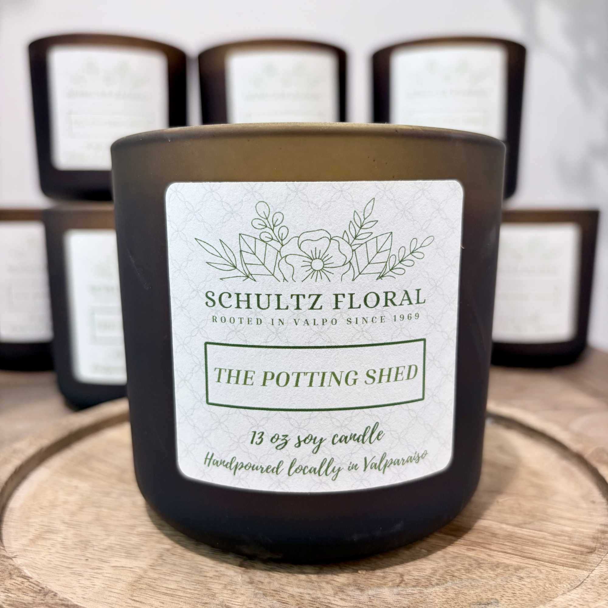 Black jar candle labeled "The Potting Shed" on a wooden tray