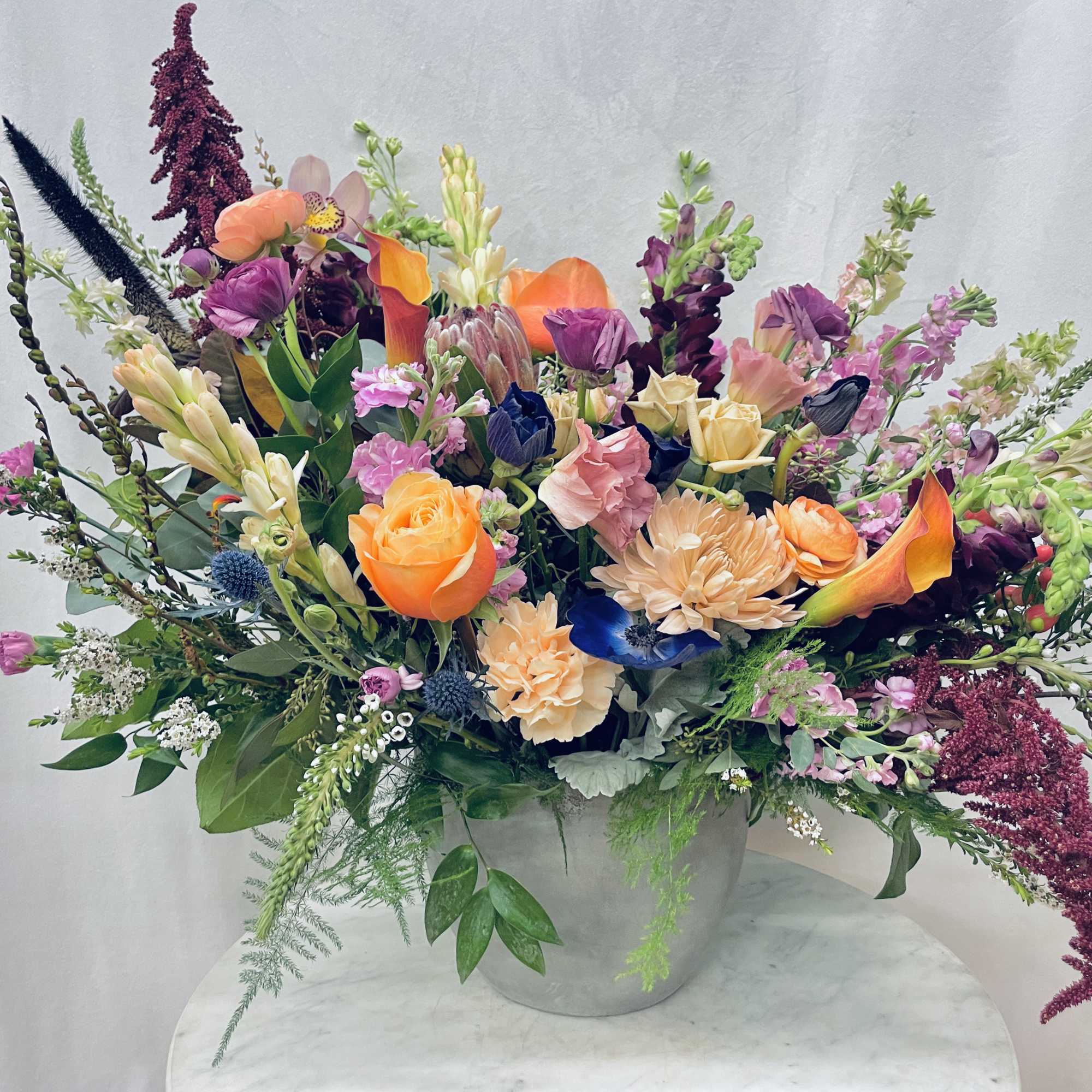 Large mixed bouquet in a gray vase with orange, purple, and pink flowers