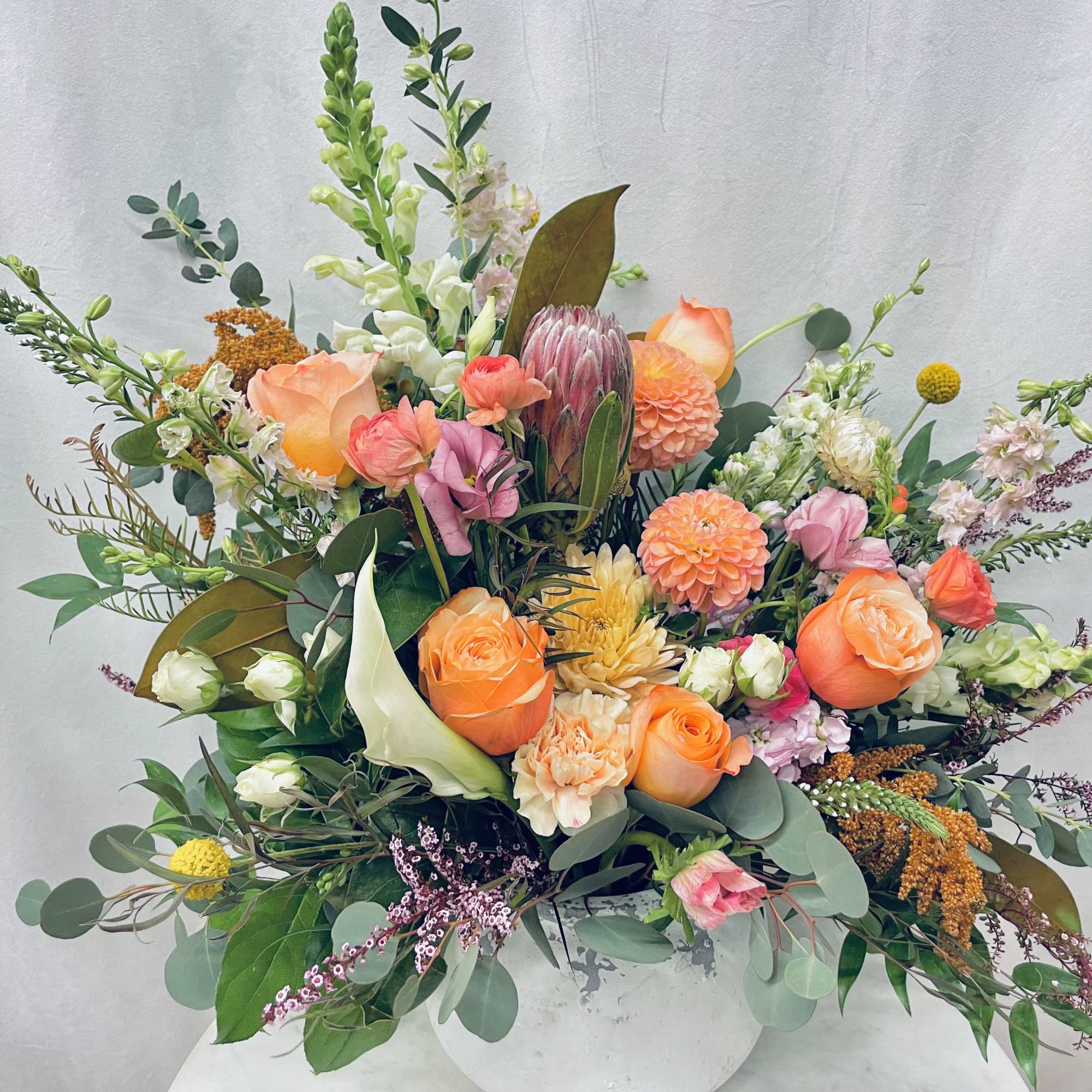 Mixed bouquet of orange, pink, and white flowers in a white vase