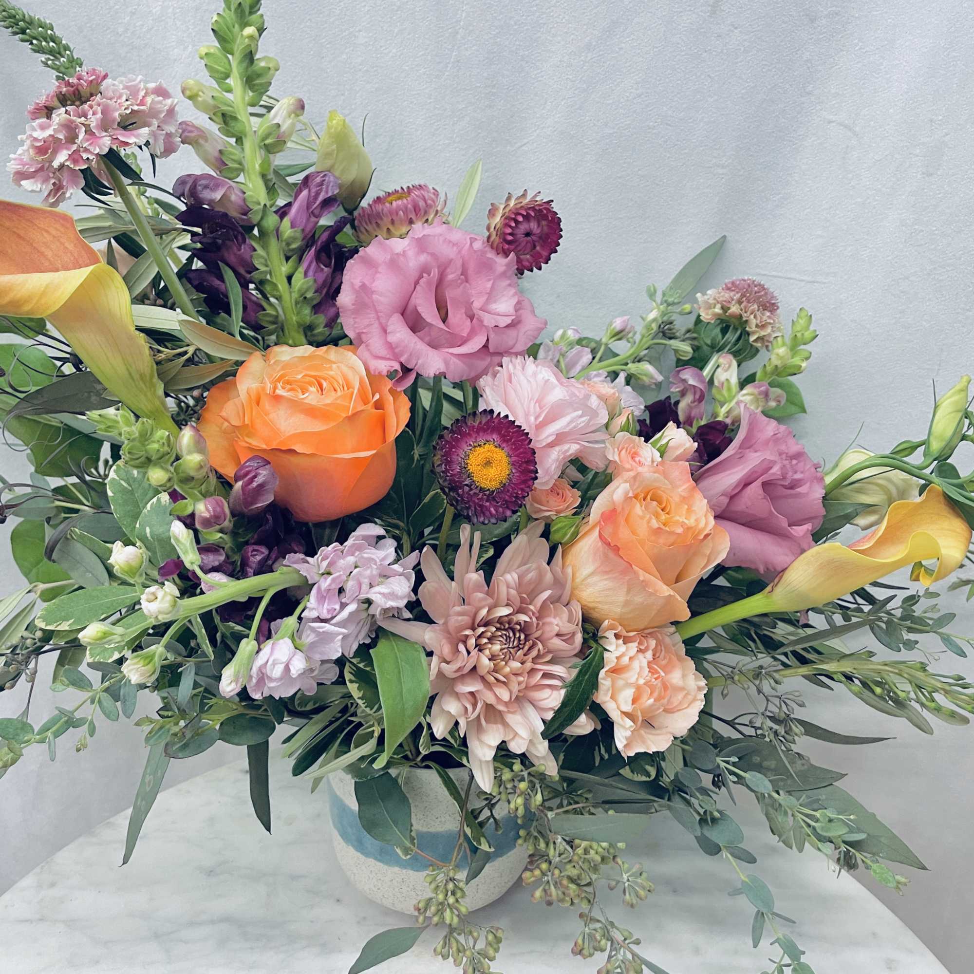 Mixed bouquet with orange roses, pink blooms, and yellow calla lilies in a ceramic vase