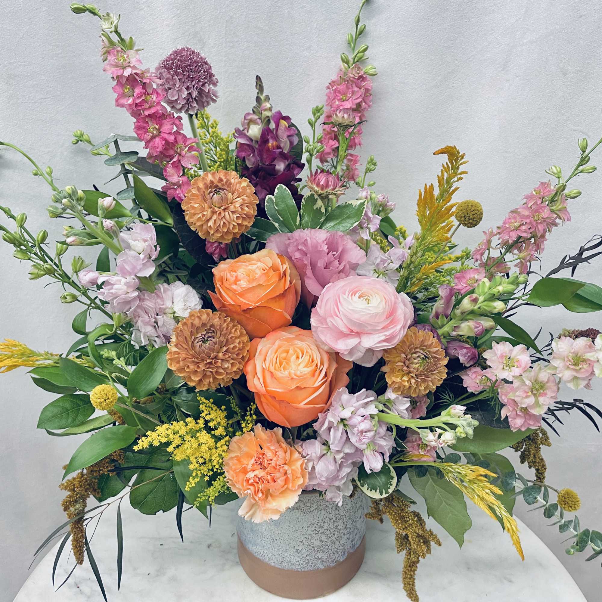 Mixed bouquet in a speckled ceramic vase with pink, orange, and yellow flowers