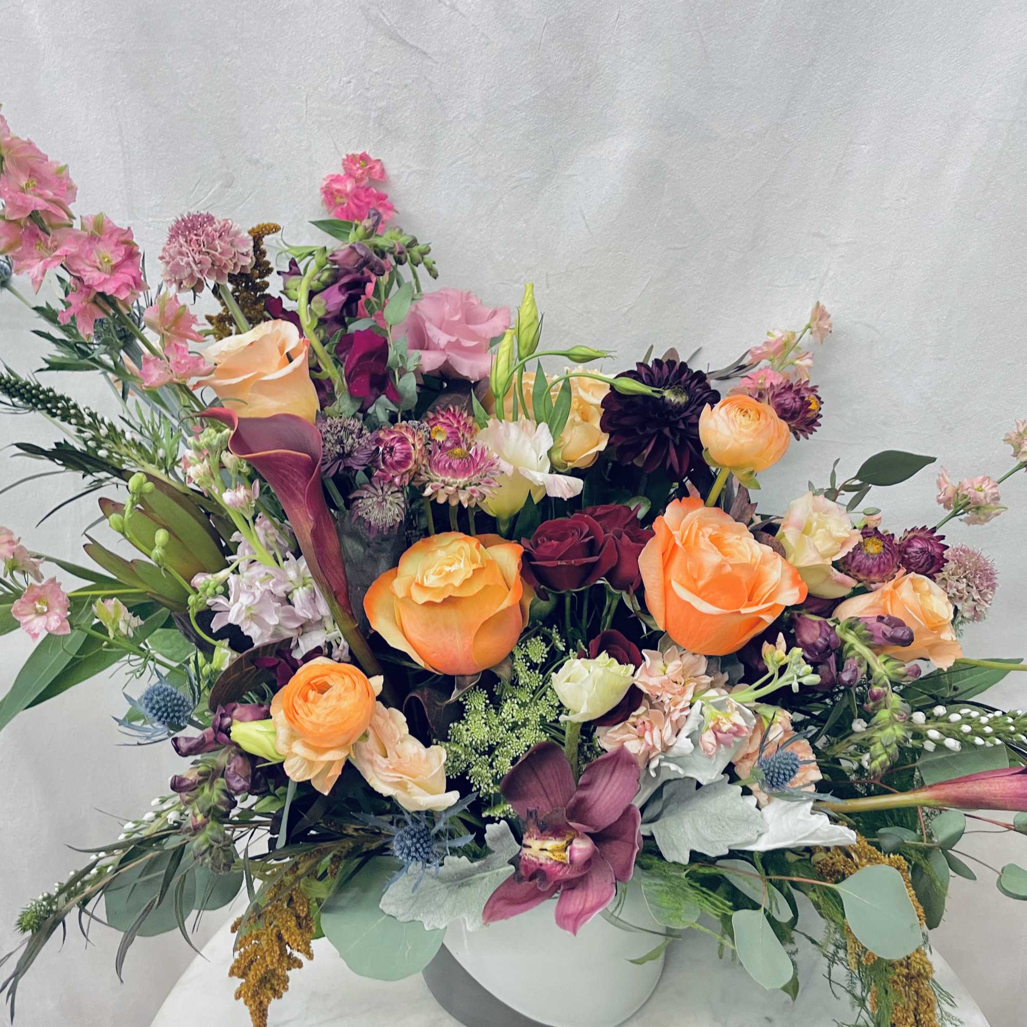 Mixed bouquet of roses, calla lilies, and assorted blooms in a white vase