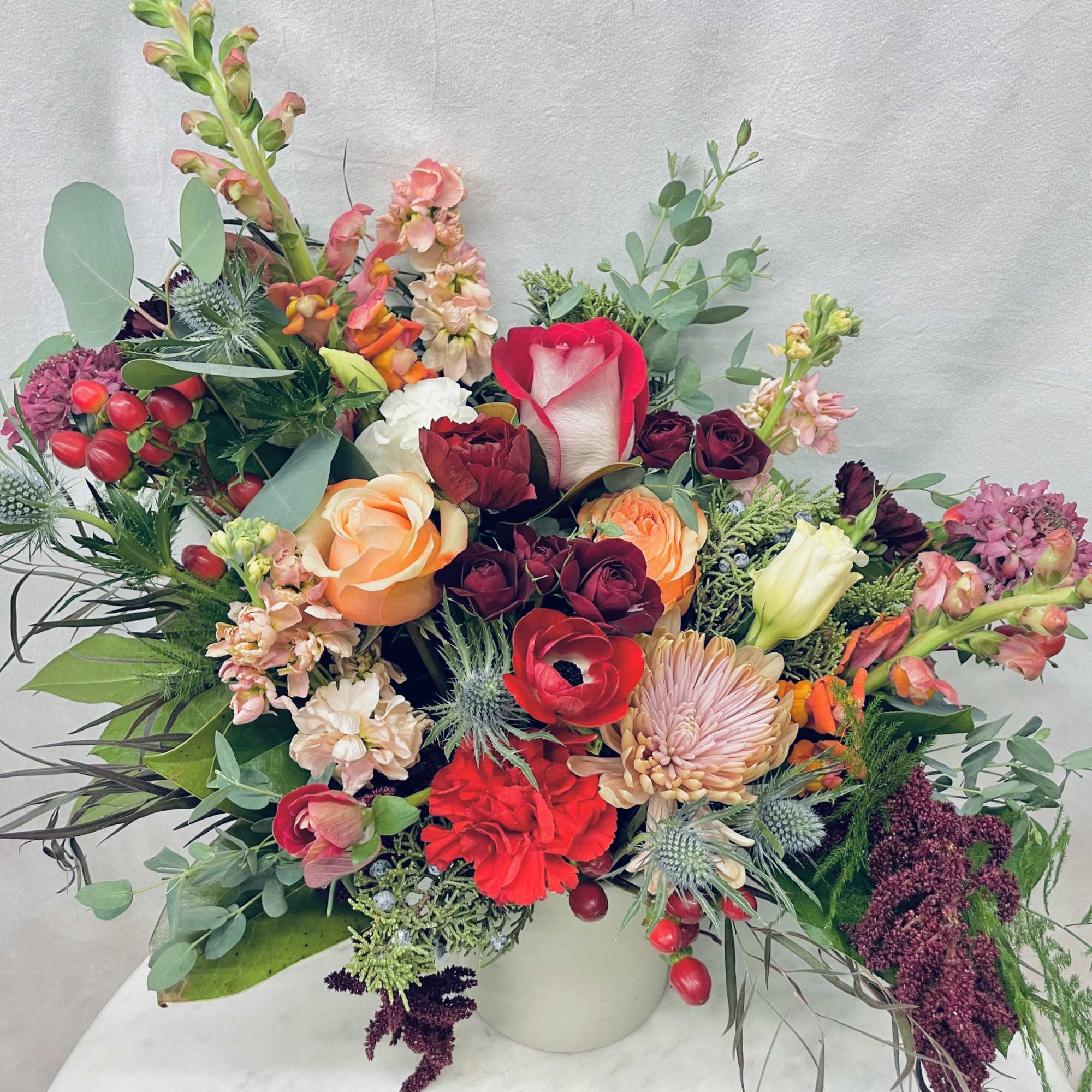 Mixed bouquet of roses, snapdragons, and other flowers in a white vase