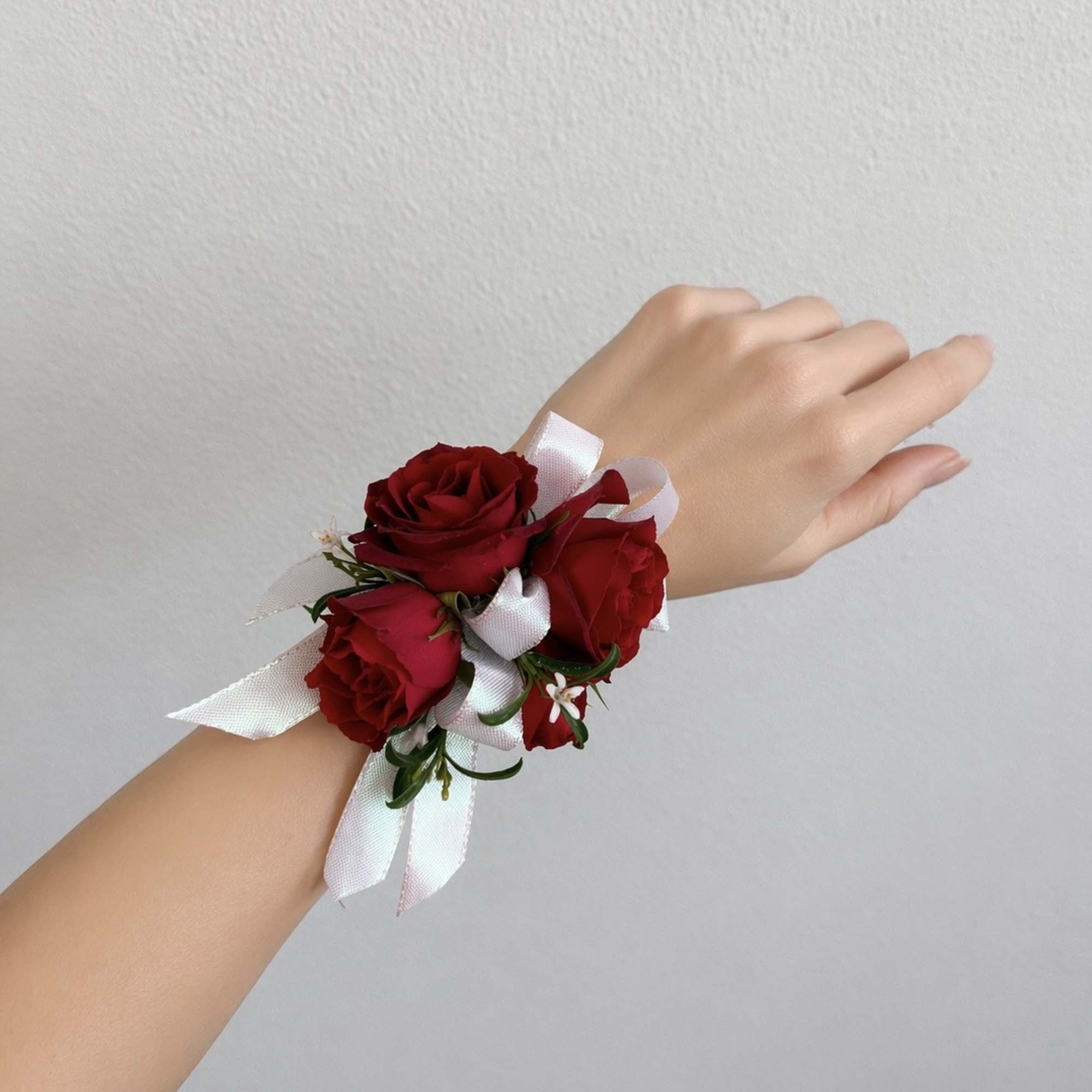 Red rose wrist corsage with white ribbon on a hand