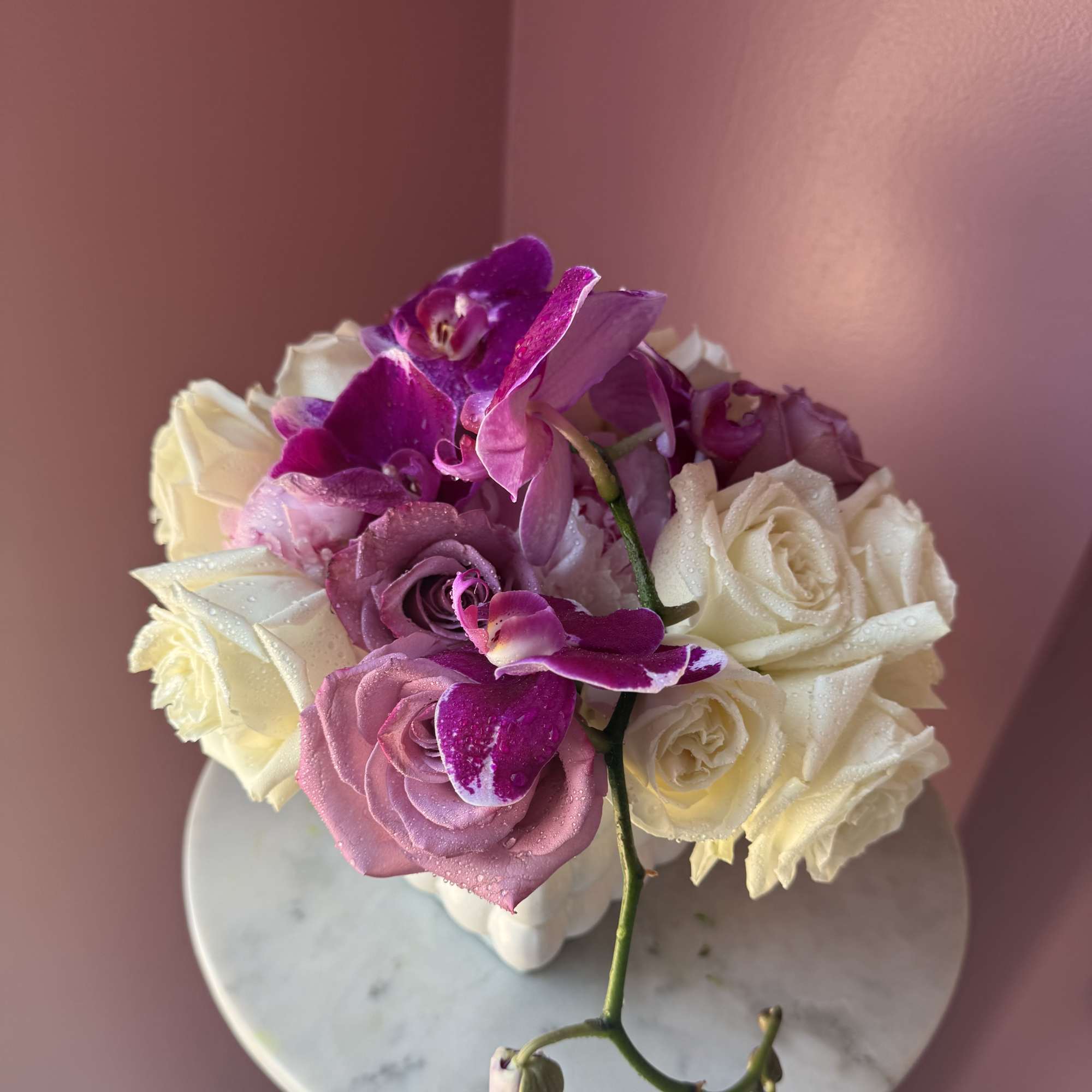 Pink and white roses with purple orchids in a white vase