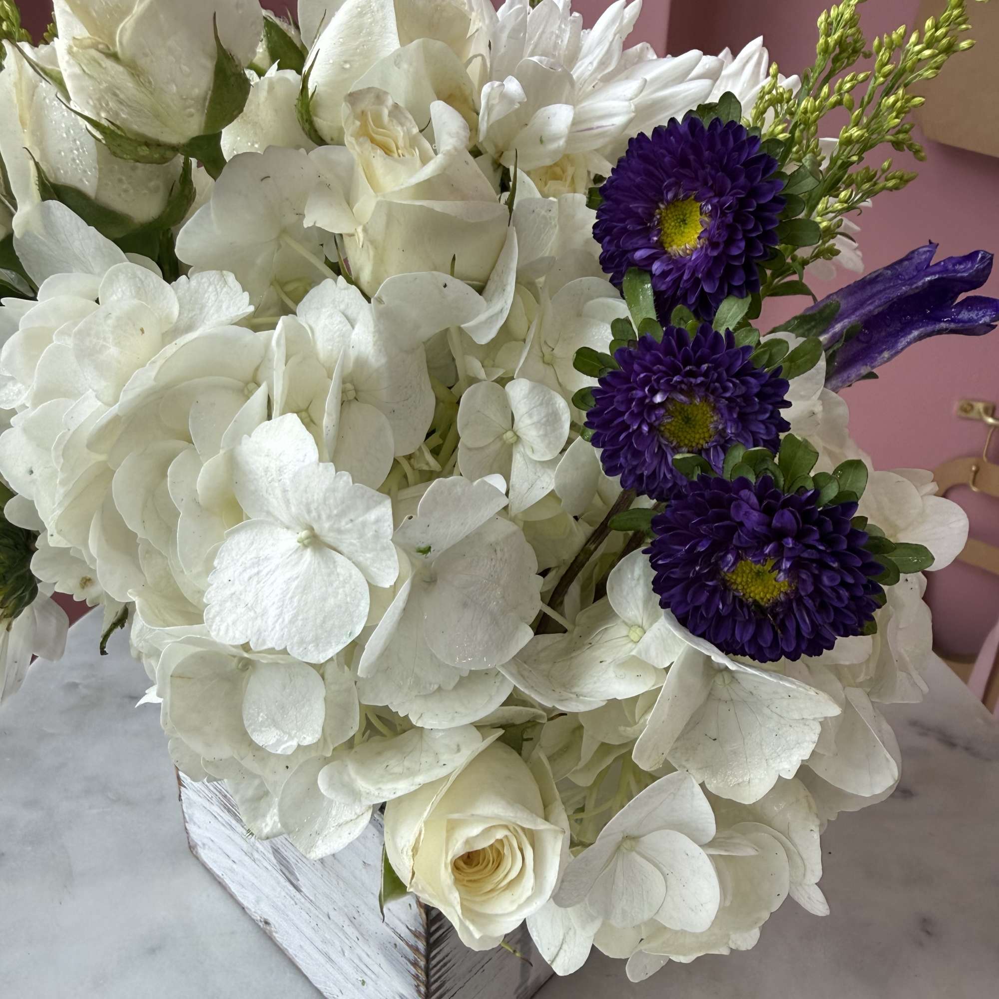 White hydrangea and roses with purple daisies in a white wooden box