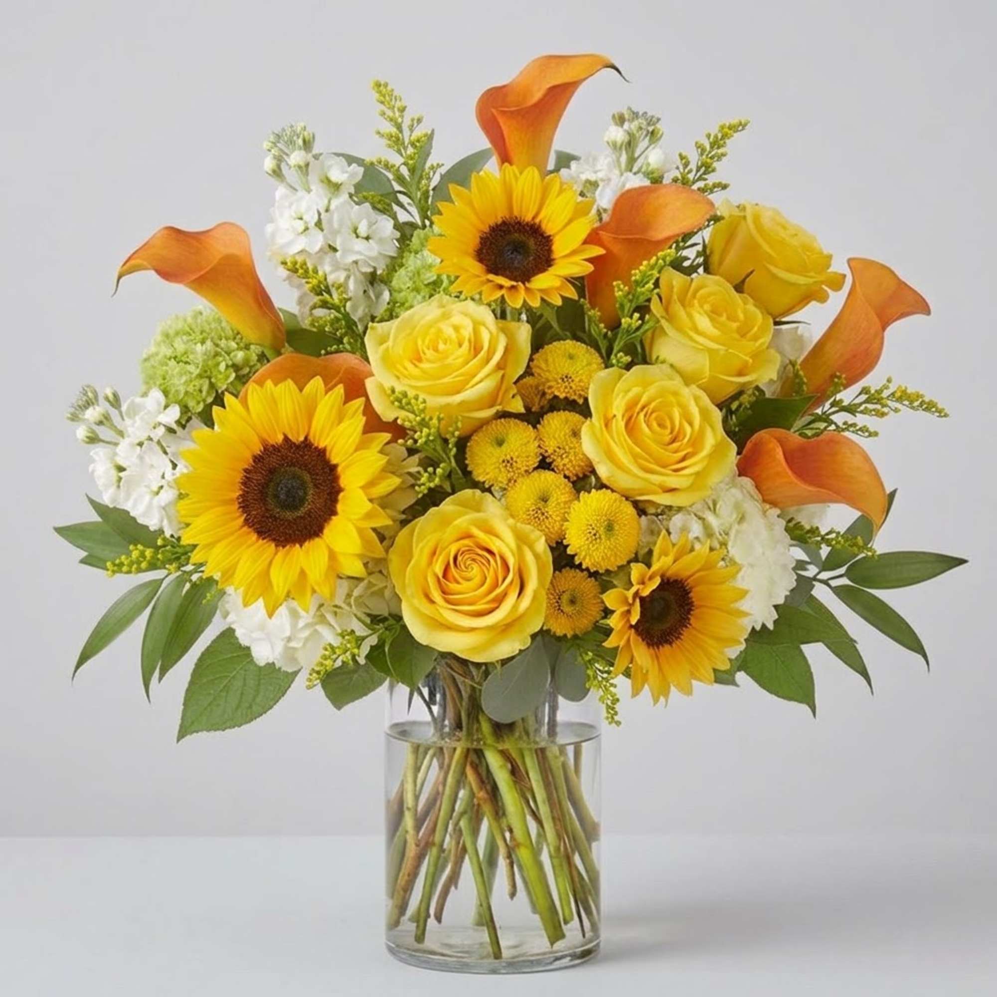 Yellow roses, sunflowers, and orange calla lilies in a glass vase
