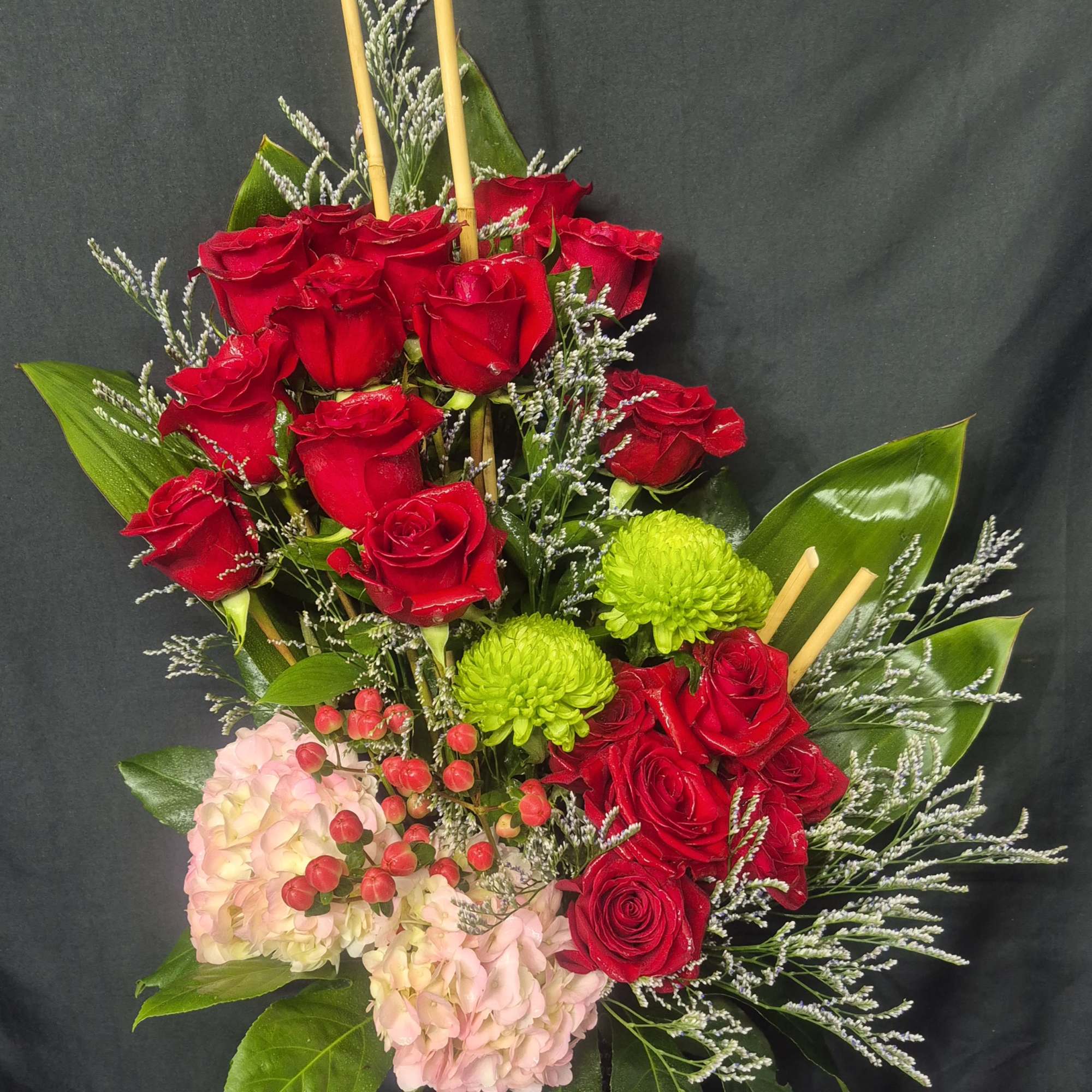 A striking and tall modern arrangement featuring vibrant red roses paired with