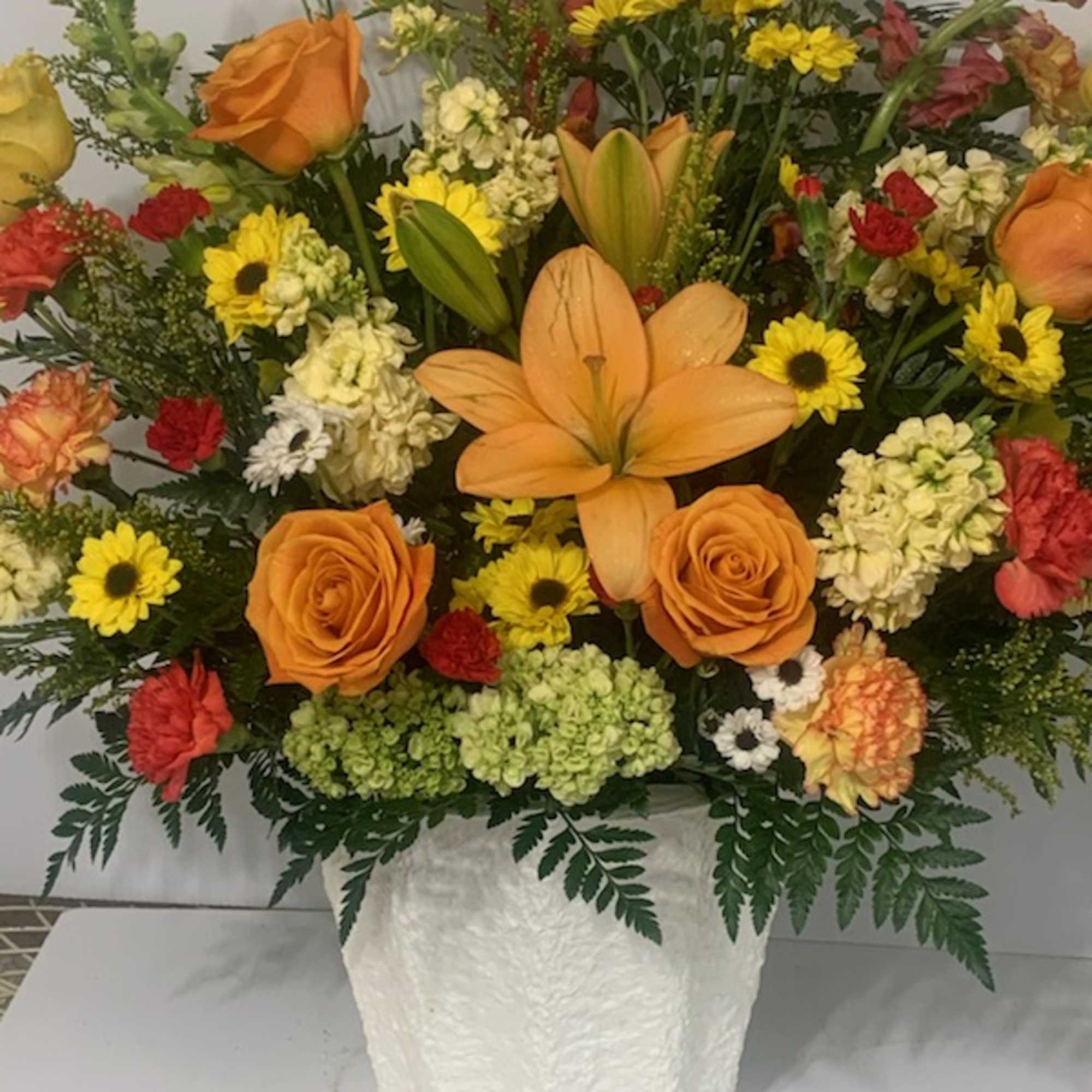 Mixed bouquet of orange roses, lilies, and yellow daisies in a white vase