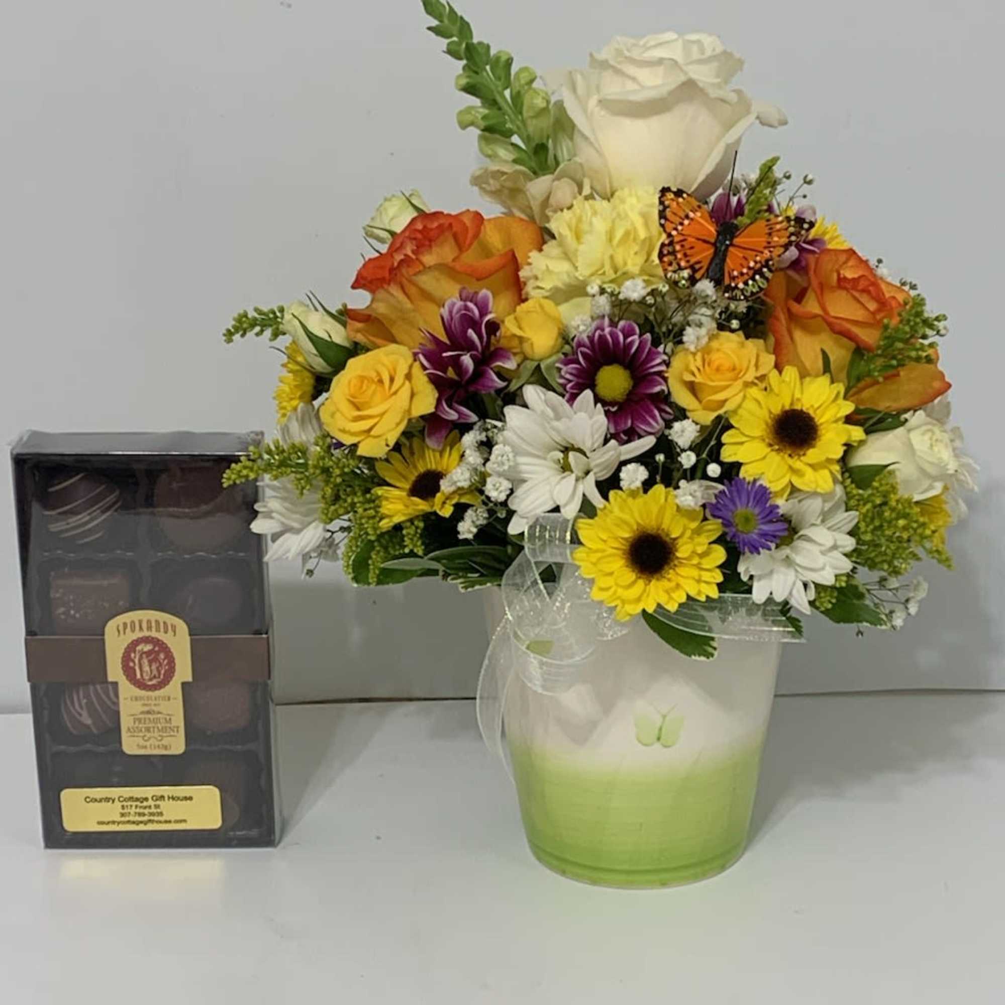 Mixed bouquet in a green glass vase beside a box of chocolates