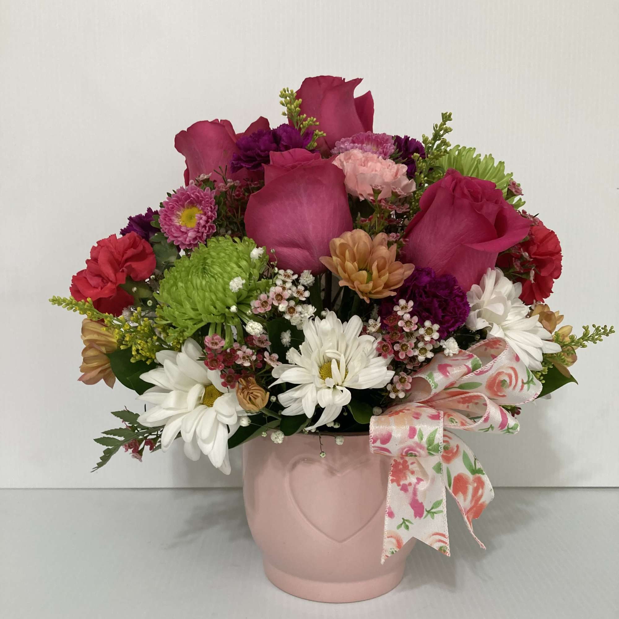 Pink and white mixed flower arrangement in a blush vase with a floral ribbon