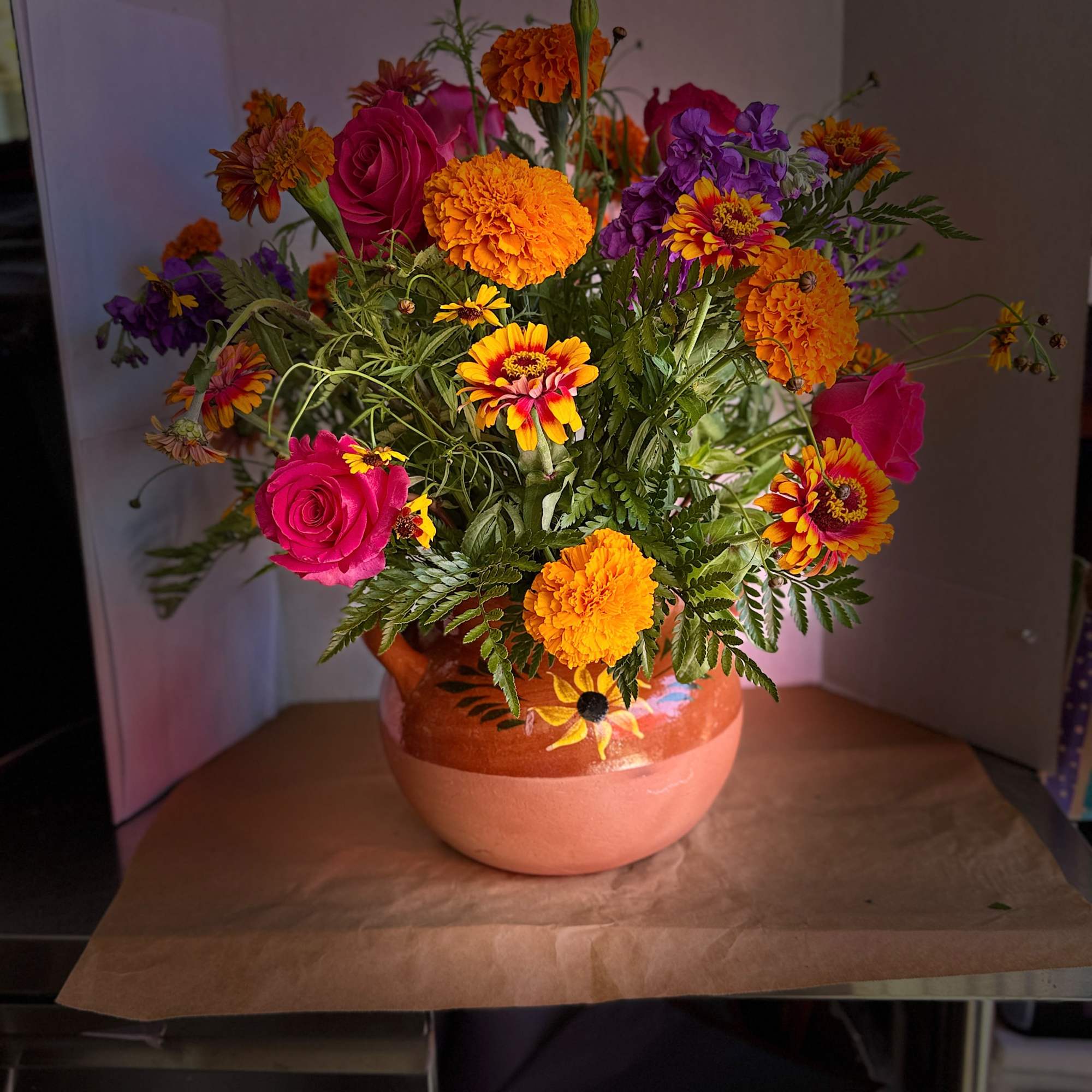 Mixed bouquet of pink roses, orange marigolds, and purple flowers in a ceramic vase