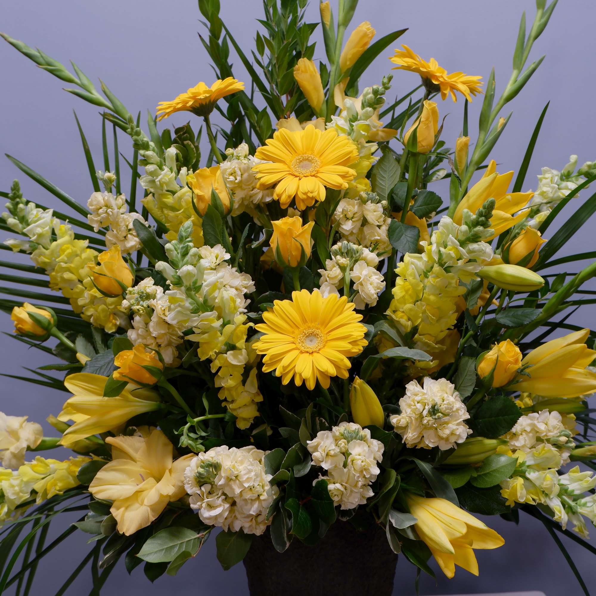 Yellow floral arrangement with gerbera daisies and lilies in a dark vase