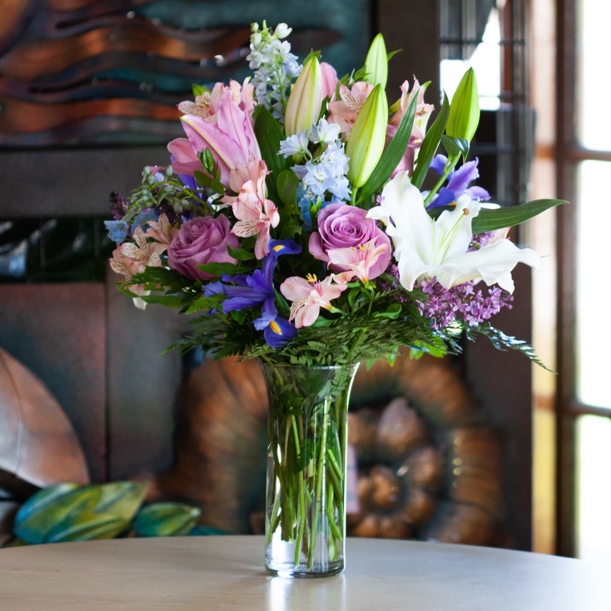 Mixed bouquet of lilies, roses, and purple flowers in a glass vase
