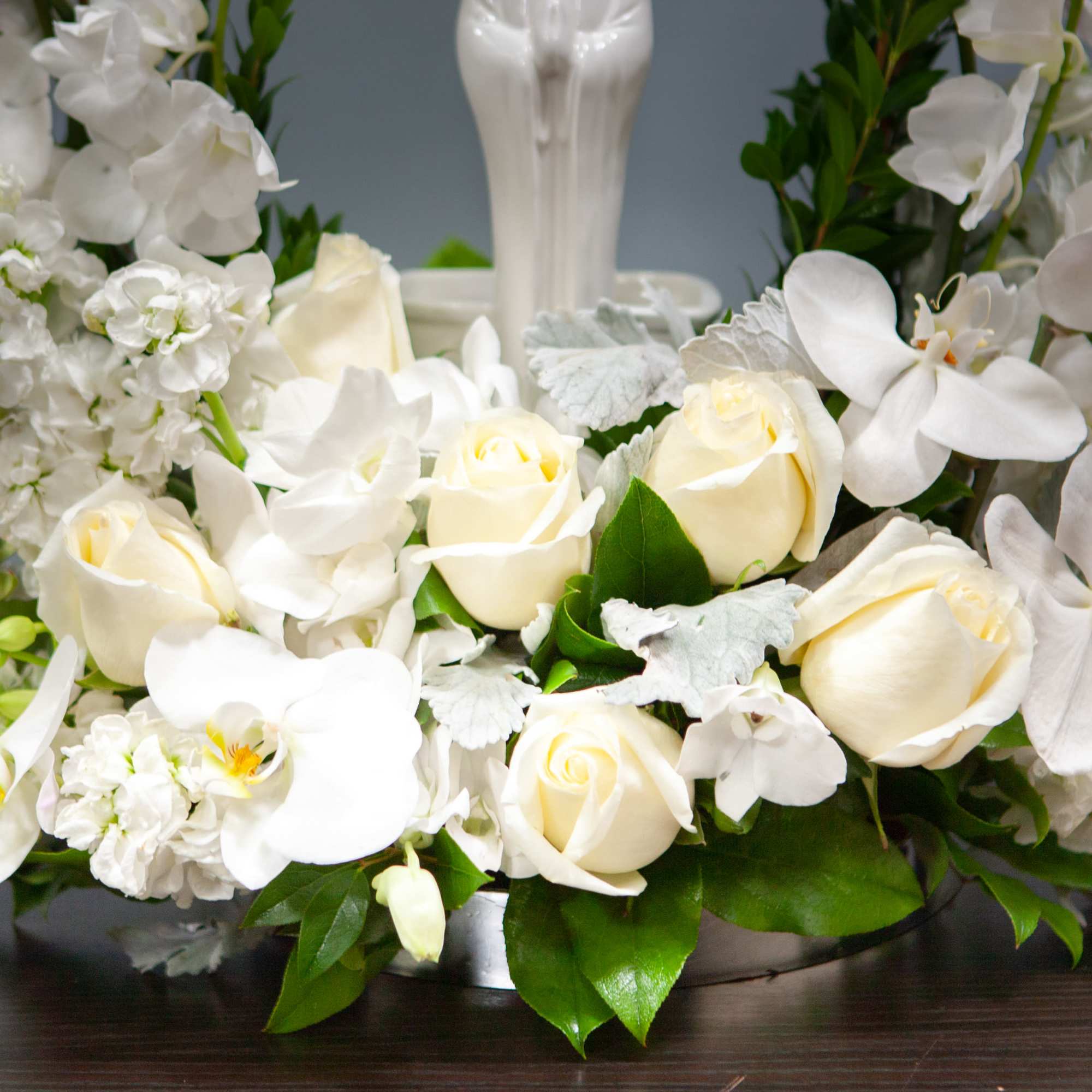 White roses and orchids arranged in a low centerpiece with greenery