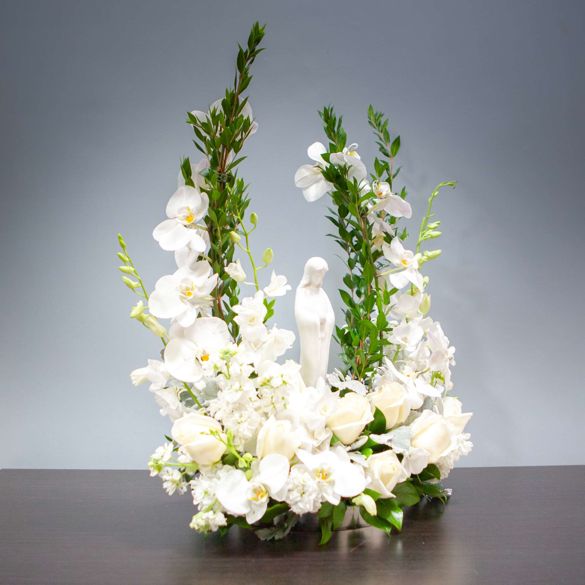 White floral arrangement with orchids and roses around a small statue