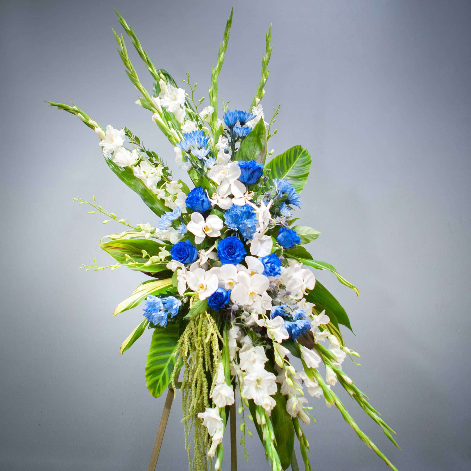 Tall blue and white floral standing spray with tropical leaves