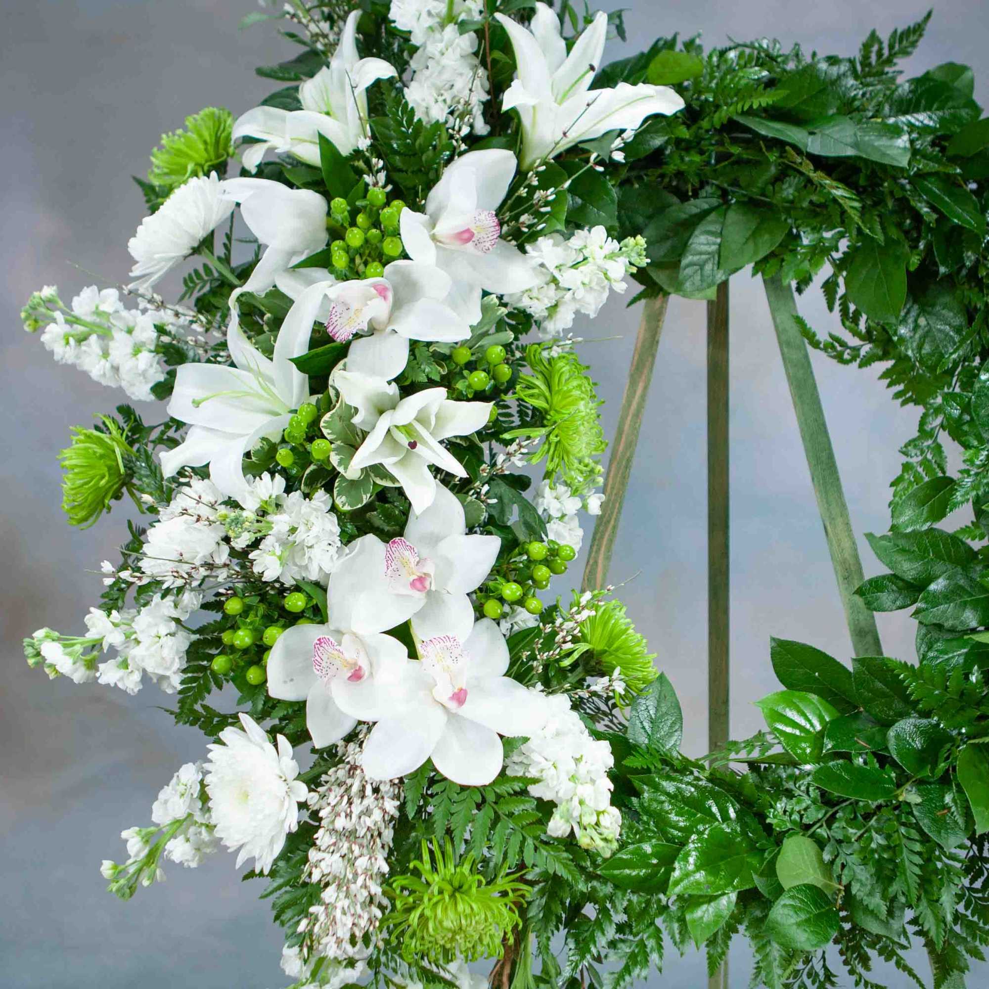 White orchid and lily wreath on a stand with dense green foliage
