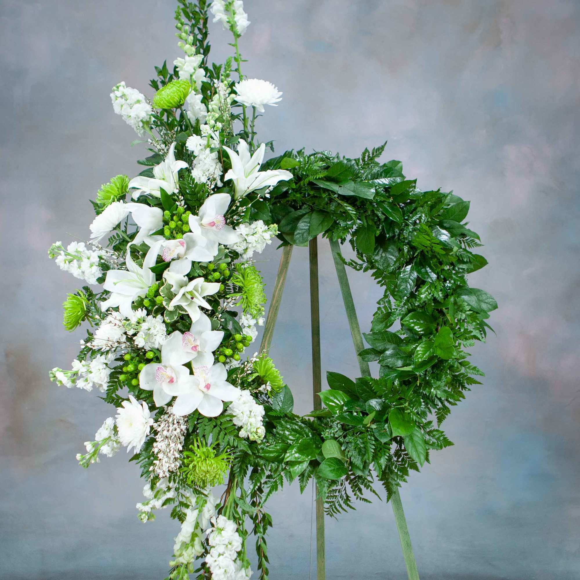 White floral wreath on a standing easel with green foliage