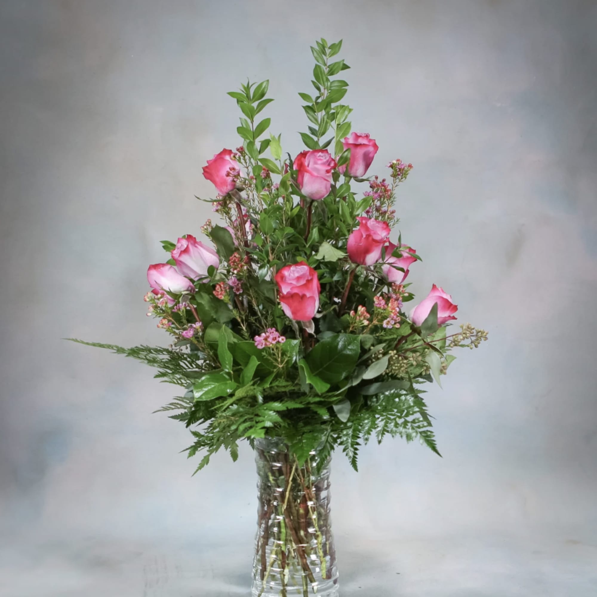Pink roses arranged in a clear glass vase with greenery