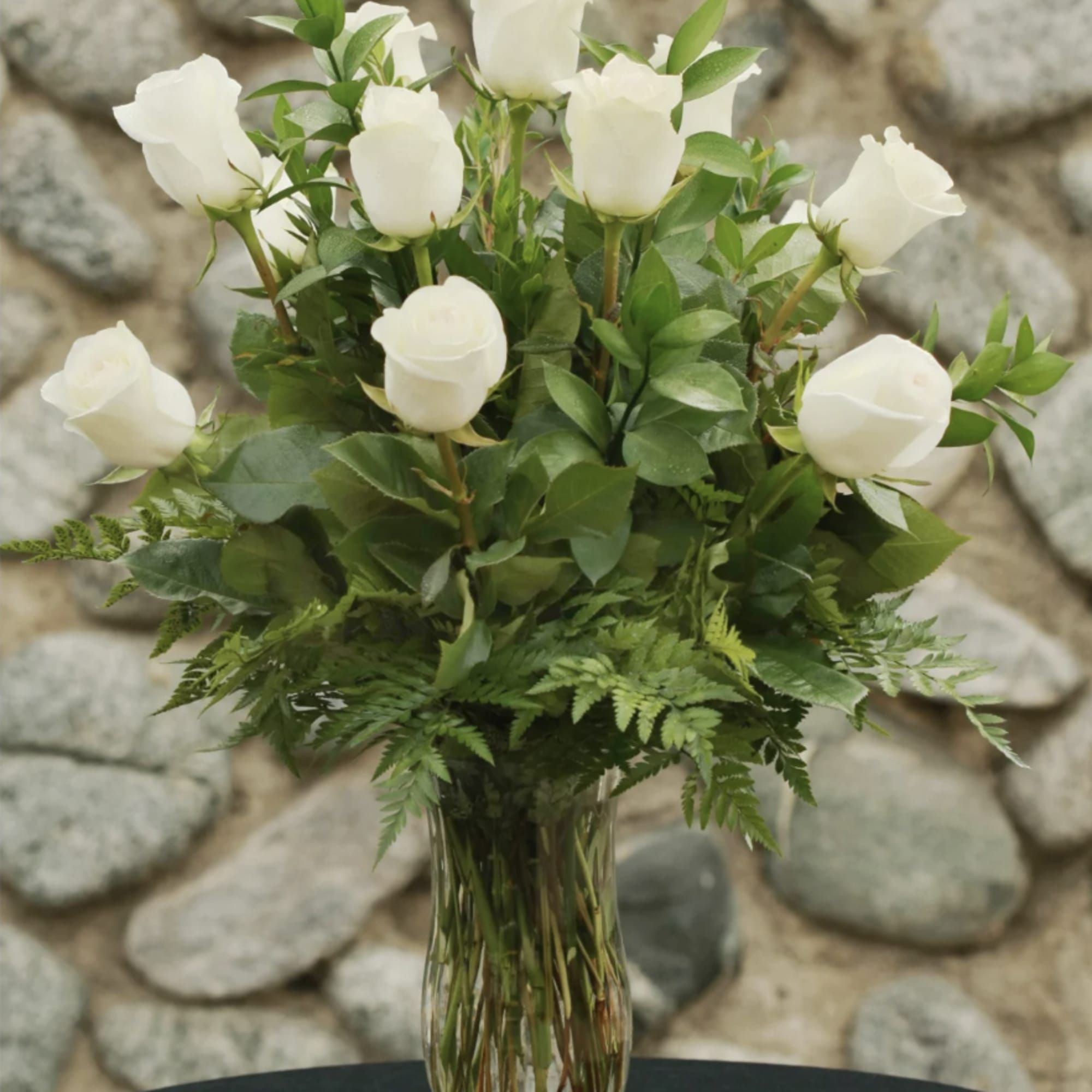 White roses arranged in a clear glass vase with fern foliage